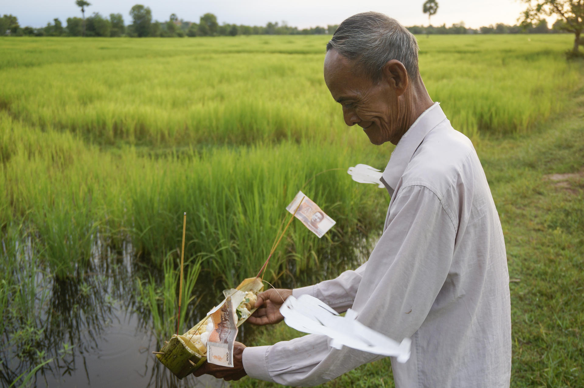 Farmer Supon's father-in-law releases paper ghosts and other offerings into his rice field in Baray village, Cambodia.