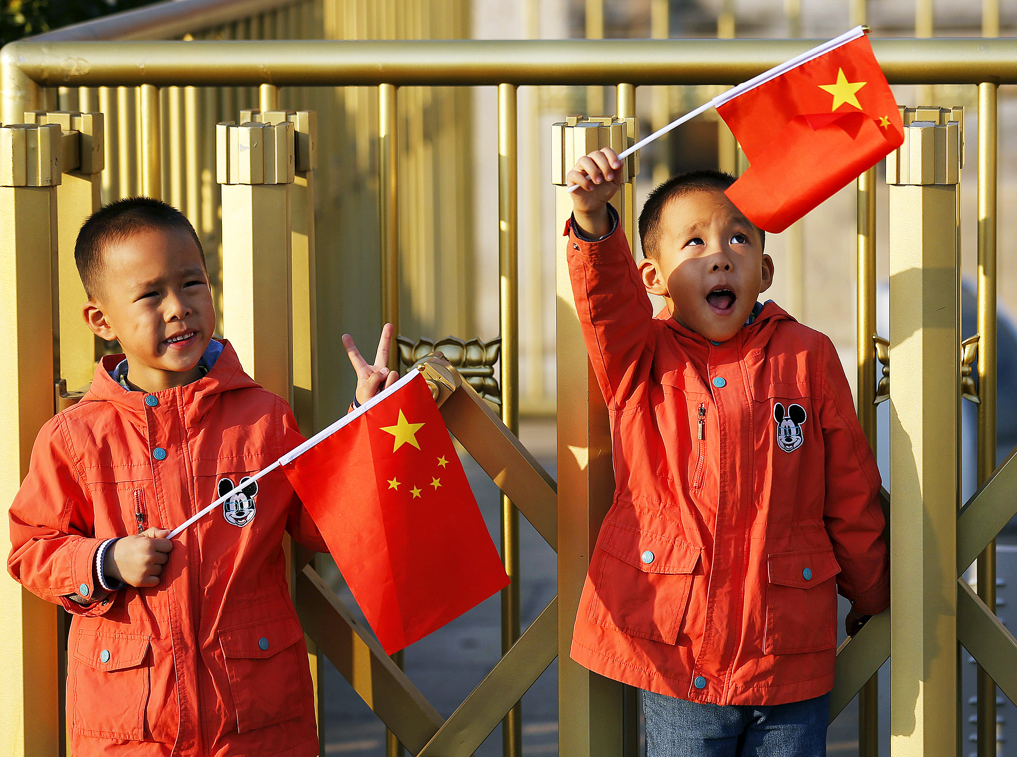 Chinese twin brothers Sun Qiyu and Sun Qichun wave national flags in Beijing on Monday. China must continue to enforce its one-child policy until new rules allowing all couples to have two children come into effect. Photo: Reuters