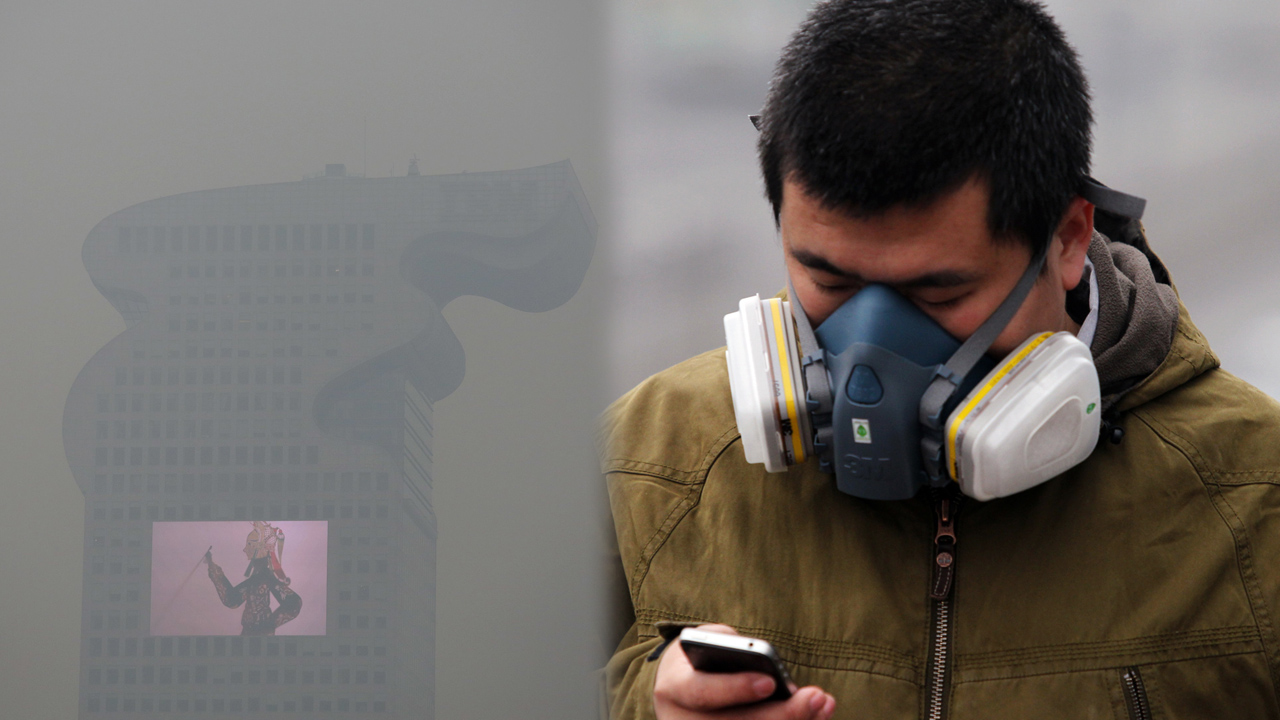 A building and a large screen are seen through tick smog in Beijing, while a man wearing a protective mask uses his phone. Photos: Reuters, Simon Song