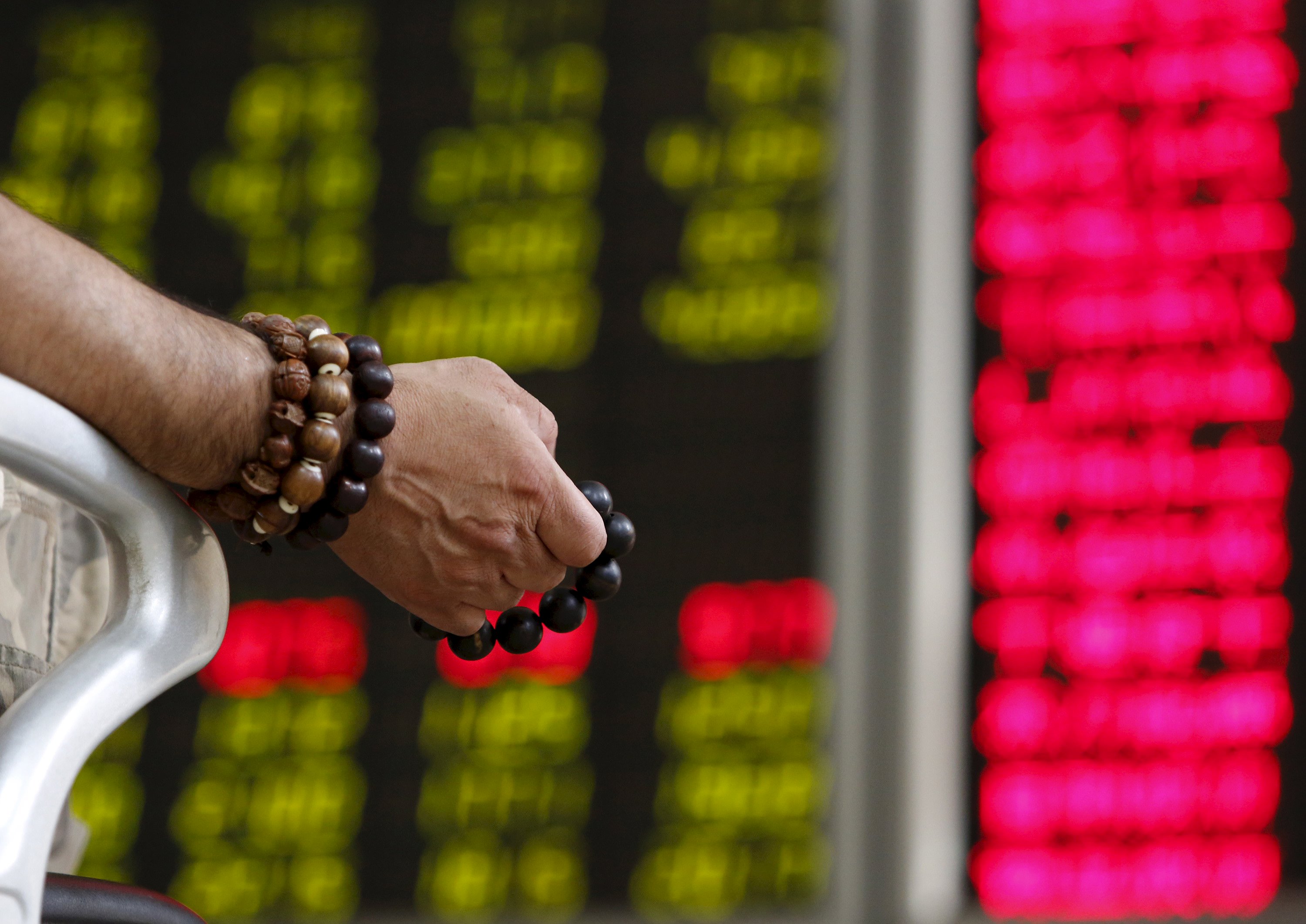 An investor holds onto prayer beads as he watches a board showing stock prices at a brokerage office in Beijing, China, in this July 6, 2015 file photo. After months trying to convince investors to come back to China's battered stock markets, there are signs authorities may be getting their wish as money starts flowing back in. China's benchmark Shanghai stock index is still a third below its June peak, but there are unquestionable signs of life in the market. REUTERS/Kim Kyung-Hoon/Files