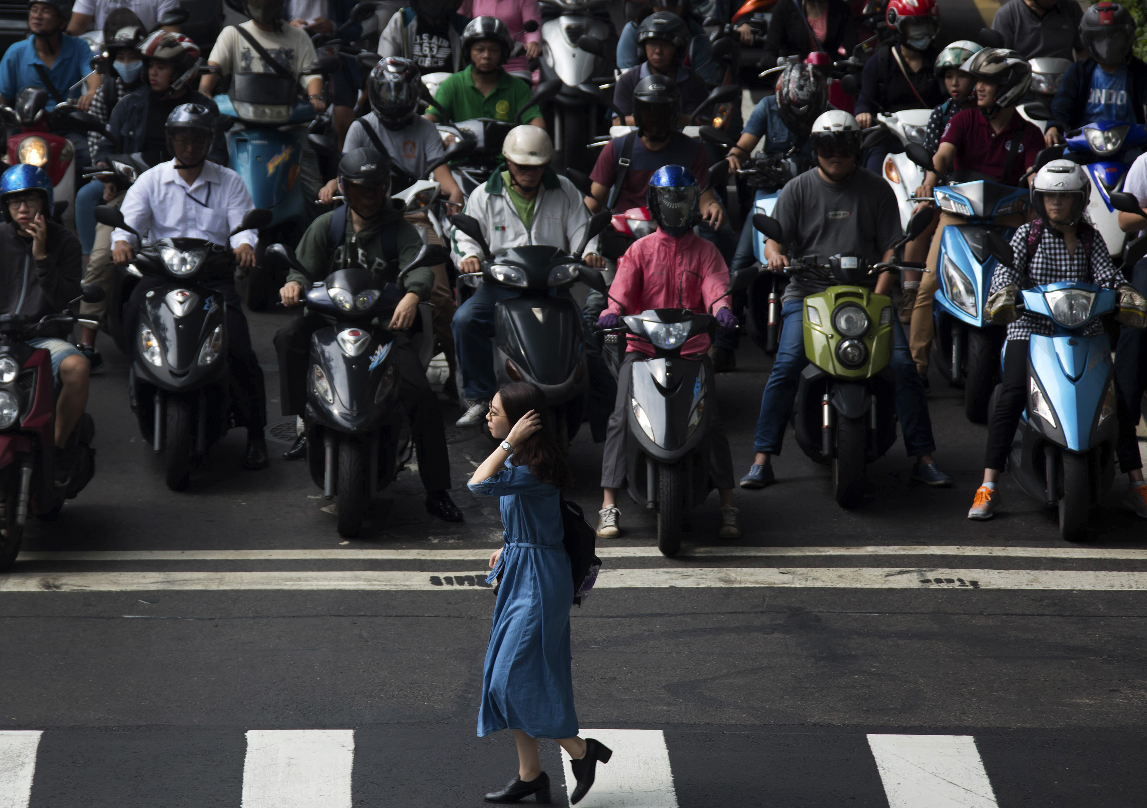 A woman crosses a road as commuters riding on motorcycles wait at a traffic stop in Taipei, Taiwan, on Monday, Nov. 9, 2015. In his meeting Saturday with outgoing Taiwanese President Ma Ying-jeou, Chinese President Xi Jinping put the relationship across the Taiwan Strait in clear terms: Stick together, and prosper. Shake things up, and sink the peace. Photographer: Tomohiro Ohsumi/Bloomberg ORG XMIT: 591161613