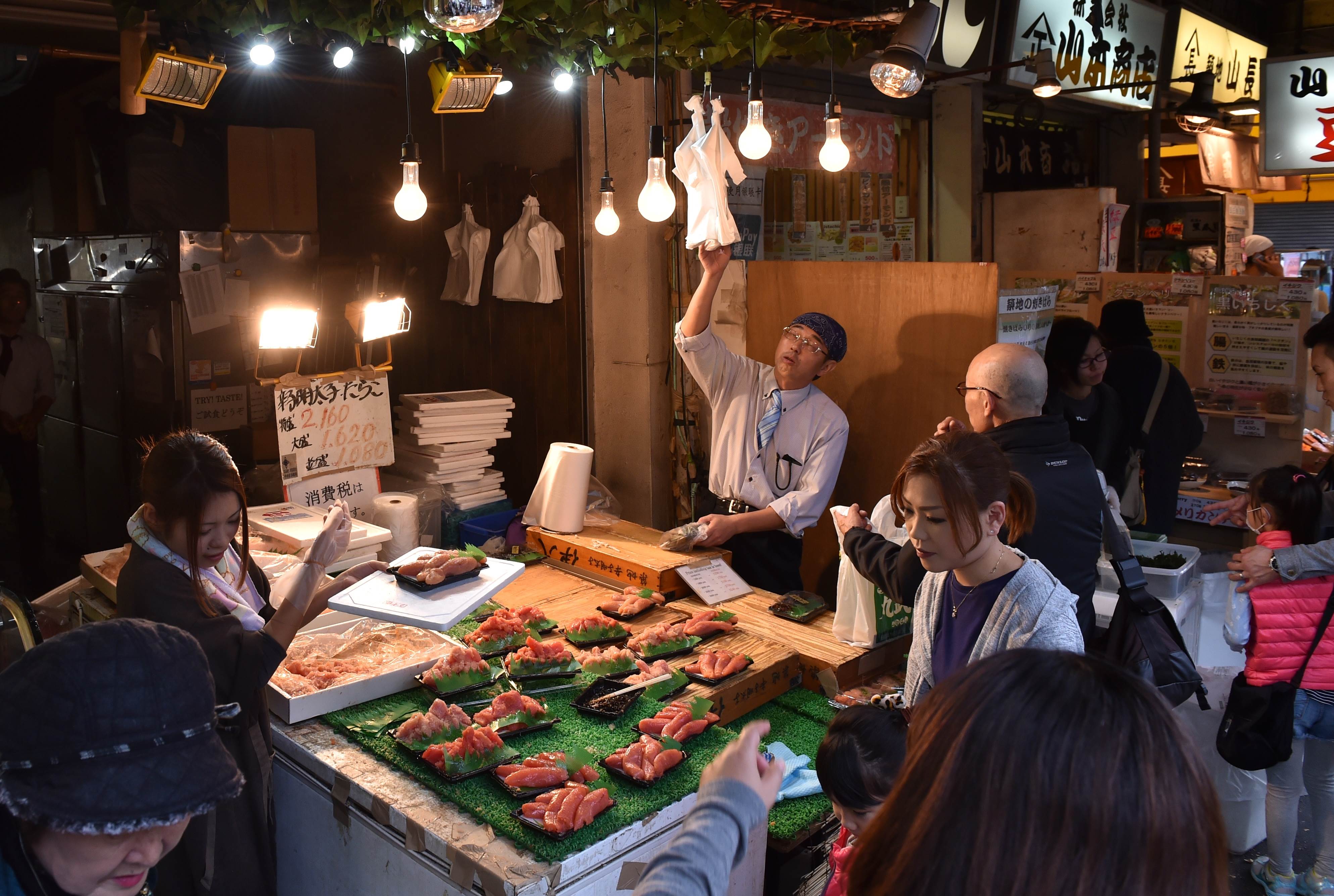 Customers gather around a seafood shop near the Tsukiji Fish Market in Tokyo on November 16, 2015. Japan's economy slipped into recession for the second time since Prime Minister Shinzo Abe came to power nearly three years ago on a vow to revive growth and end chronic deflation, government figures showed November 16. AFP PHOTO / KAZUHIRO NOGI