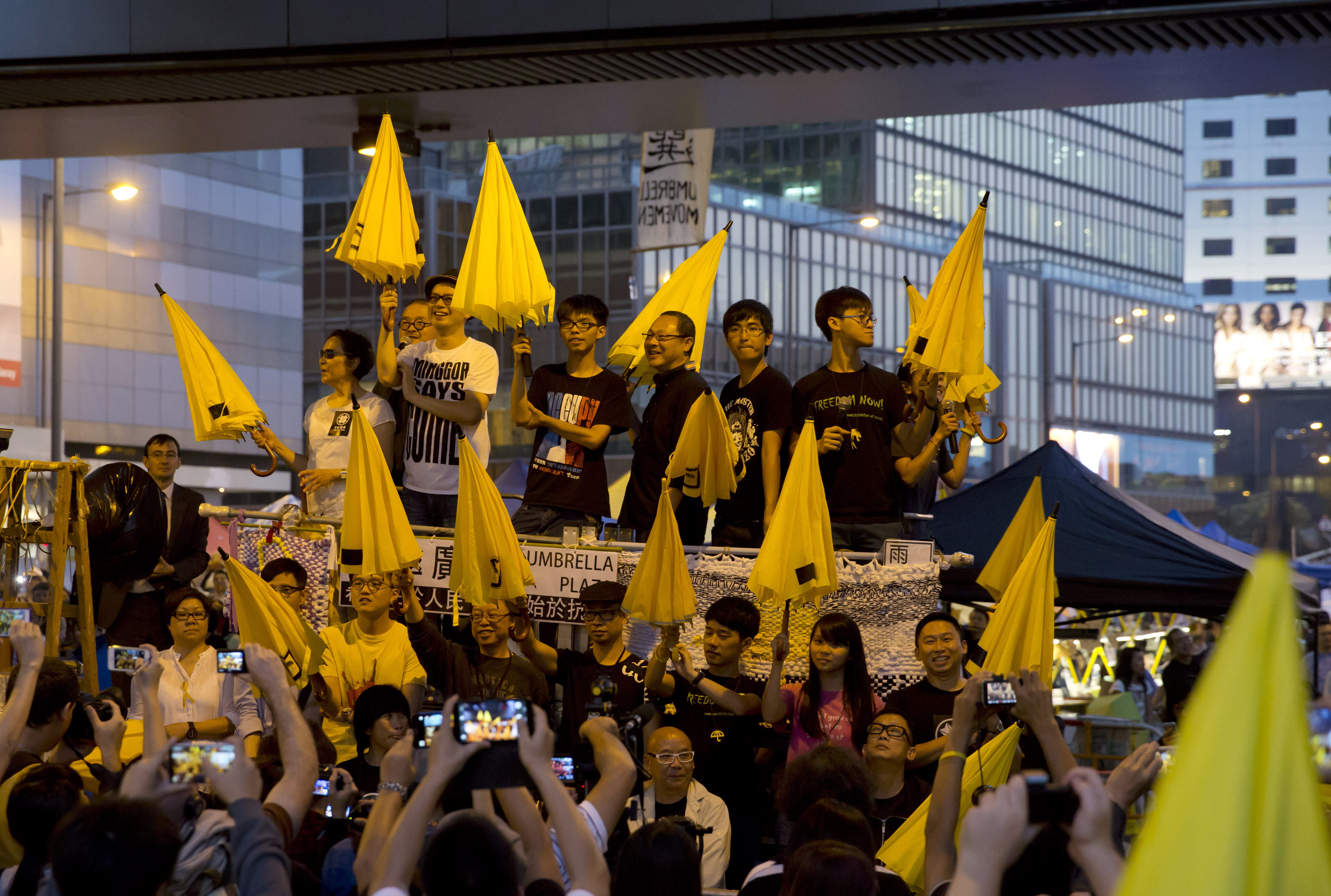 Standing on the stage in front of protesters, Hong Kong actress Deanie Yip, left, and singer Anthony Wong, second left, join student leader Joshua Wong, third left, founder of the Occupy Central civil disobedience movement Benny Tai, third right, and students leaders, Alex Chow, second right, and Tommy Cheung, as they raise umbrellas at a rally in the occupied areas outside government headquarters in Hong Kong's Admiralty Tuesday, Oct. 28, 2014. Pro-democracy protests in Hong Kong stretched into a fourth week, as student leaders pushing for a greater say in choosing the territory's chief executive met with government officials but agreed on little. (AP Photo/Kin Cheung)