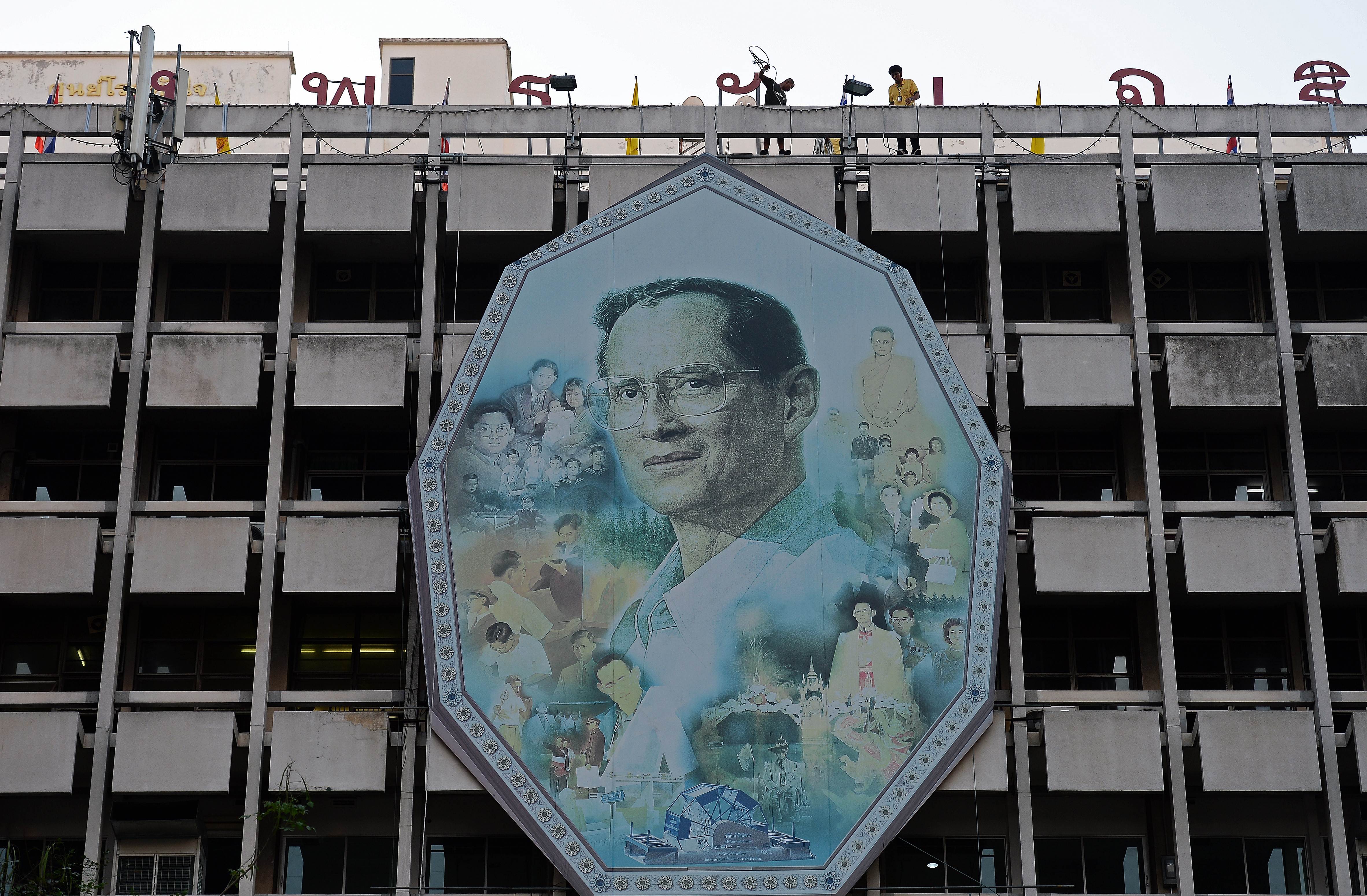 Workers use ropes to remove a portrait of King Bhumibol Adulyadej and install a new one on a facade as people gather at the Siriraj hospital where the King has been staying for months on the eve of his 88th birthday in Bangkok on December 4, 2015. Thai King Bhumibol, the world's longest reigning monarch who is regarded as a demi-god by many Thais and considered a unifying force in a politically turbulent nation, will turn 88 on December 5, 2015. AFP PHOTO / Christophe ARCHAMBAULT