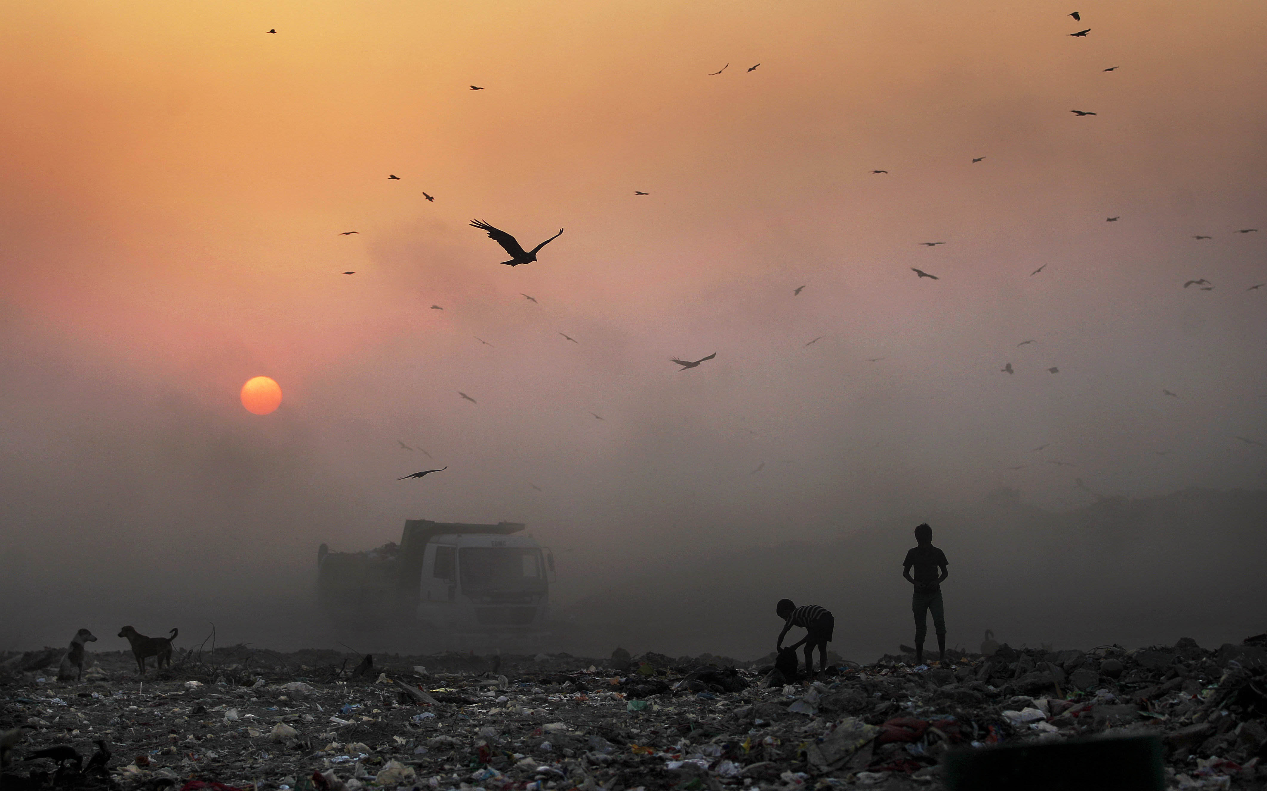 FILE- In this Oct. 17, 2014, file photo, a thick blanket of smoke is seen against the setting sun as young ragpickers search for reusable material at a garbage dump in New Delhi, India. New Delhi city is imposing new rules to reduce its notoriously snarled traffic and fight extreme air pollution that has earned India’s capital the title of world's most polluted city. (AP Photo/Altaf Qadri)