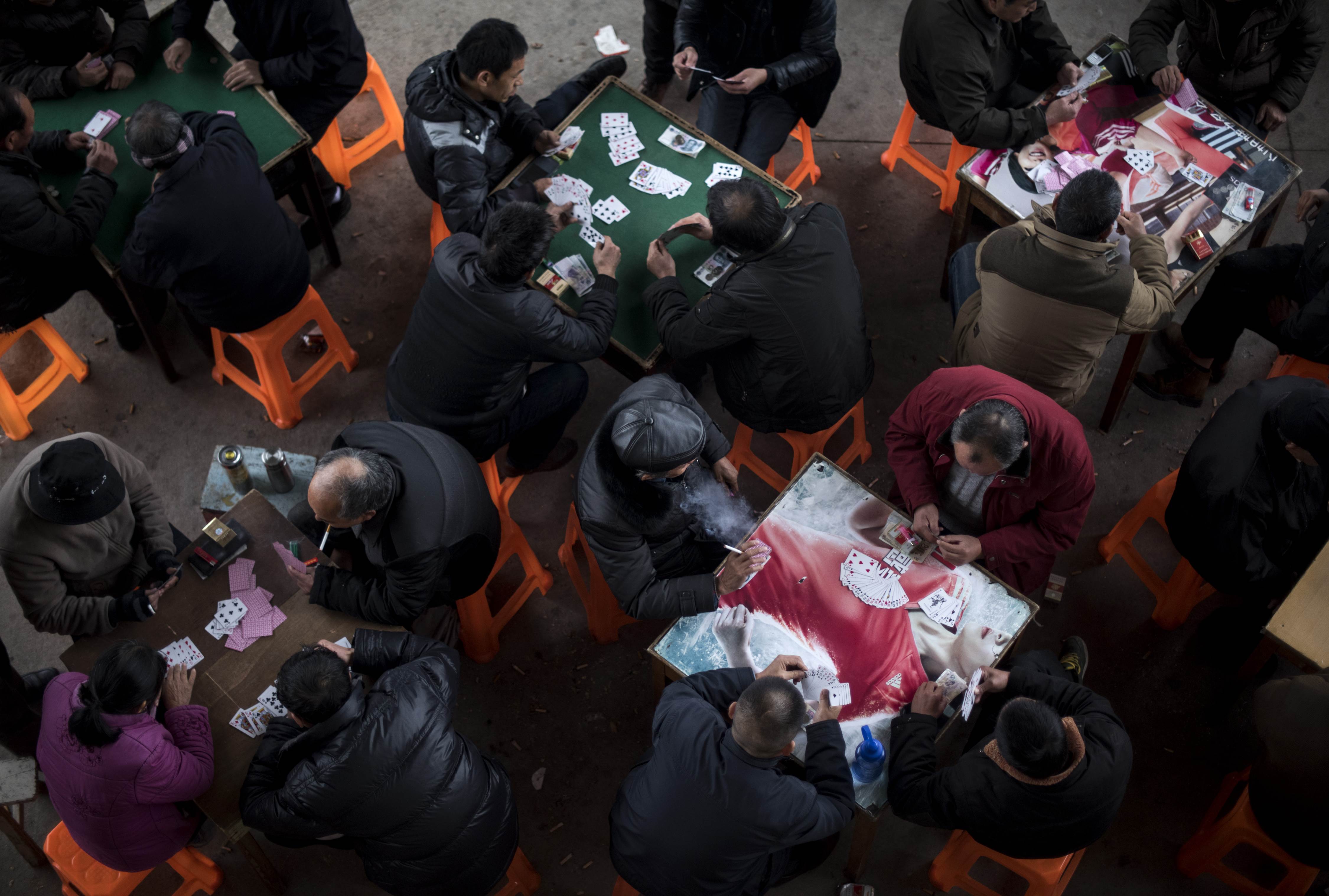 This picture taken on December 9, 2015 shows men playing cards under a bridge next to the Xin'an River on a rainy day in Huangshan city, southern Anhui province. China's consumer inflation rate edged up in November, official data showed on December 9, while factory gate price falls lingered at a six-year low as the world's second-largest economy grapples with slowing growth. AFP PHOTO / JOHANNES EISELE
