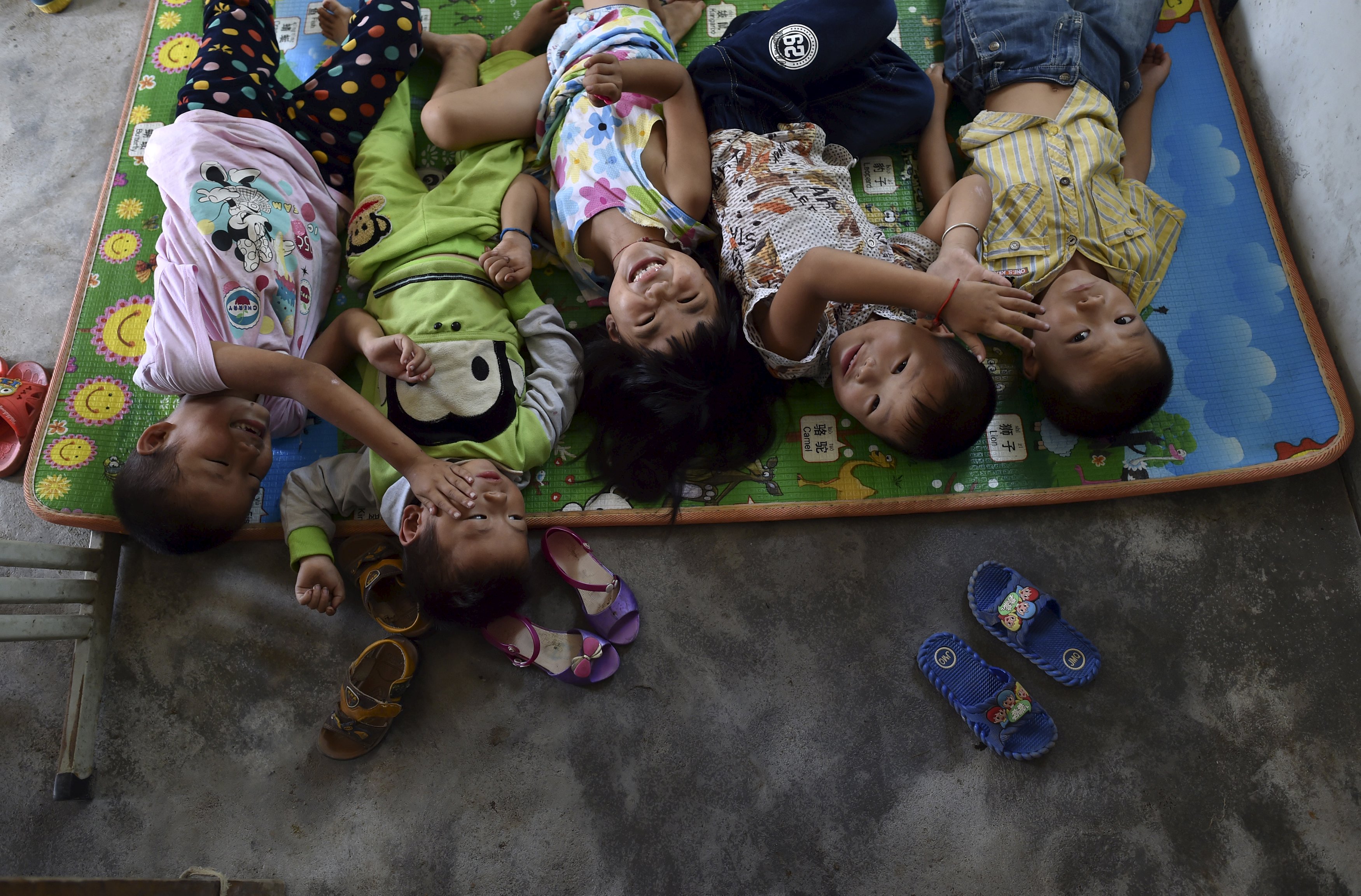 Students play as they sleep on a mat on the ground at Dalu primary school in Gucheng township of Hefei, Anhui province, China, September 8, 2015. The school, opened in 2006 and has never acquired a legal license, may face a shutdown order from the government. There are currently over 160 students in the school, mostly "leftover children", whose parents left their hometown to earn a living, local media reported. Picture taken September 8, 2015. REUTERS/Stringer CHINA OUT. NO COMMERCIAL OR EDITORIAL SALES IN CHINA