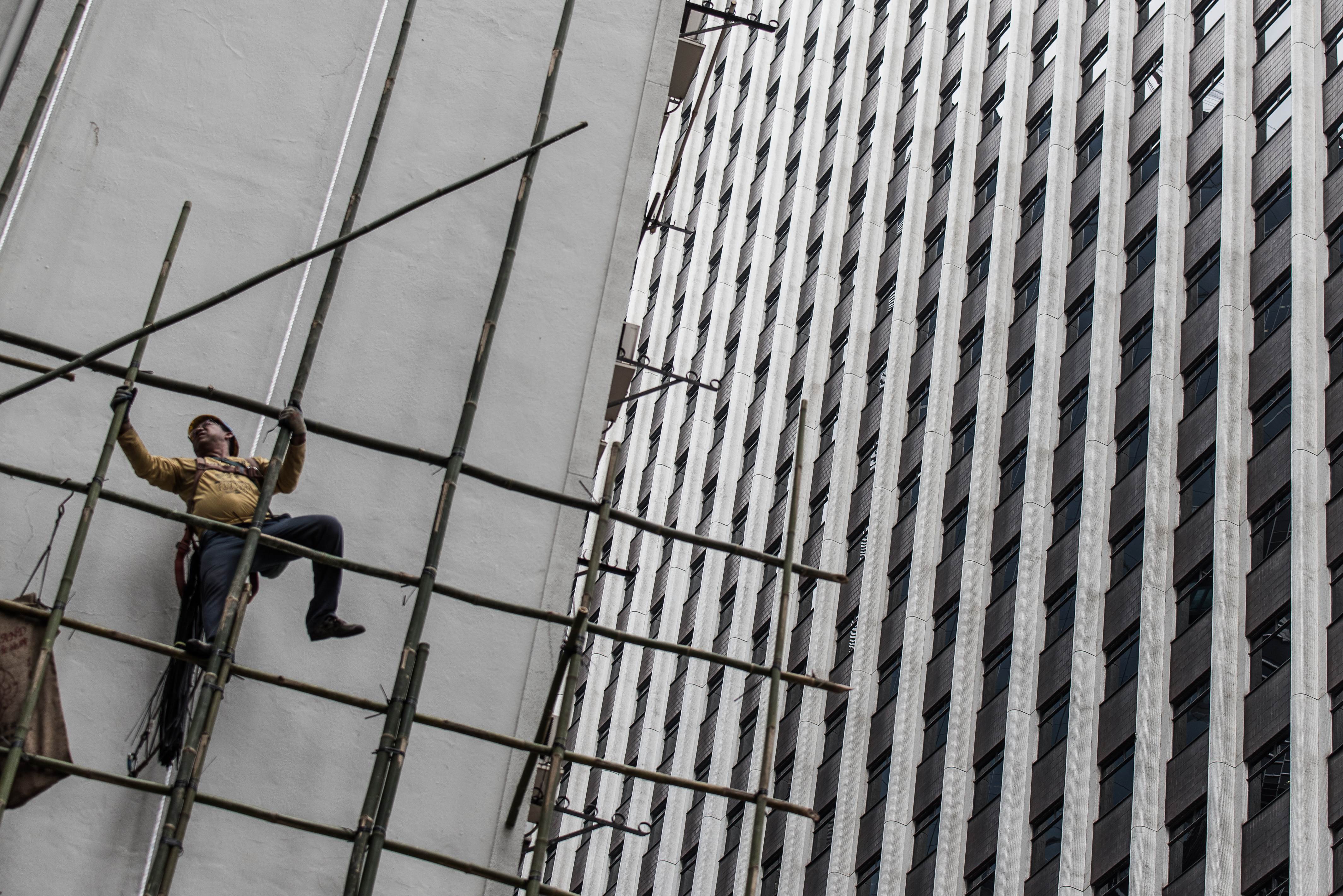 A worker balances on a bamboo scaffolding in Hong Kong on December 3, 2015. Hong Kong's bamboo scaffolders have risen above predictions that their trade would disappear, remaining a common sight high above the streets of the city, scaling the sides of towering, ultra-modern steel and glass buildings on traditional bamboo poles linked through ancient design concepts. AFP PHOTO / Philippe Lopez