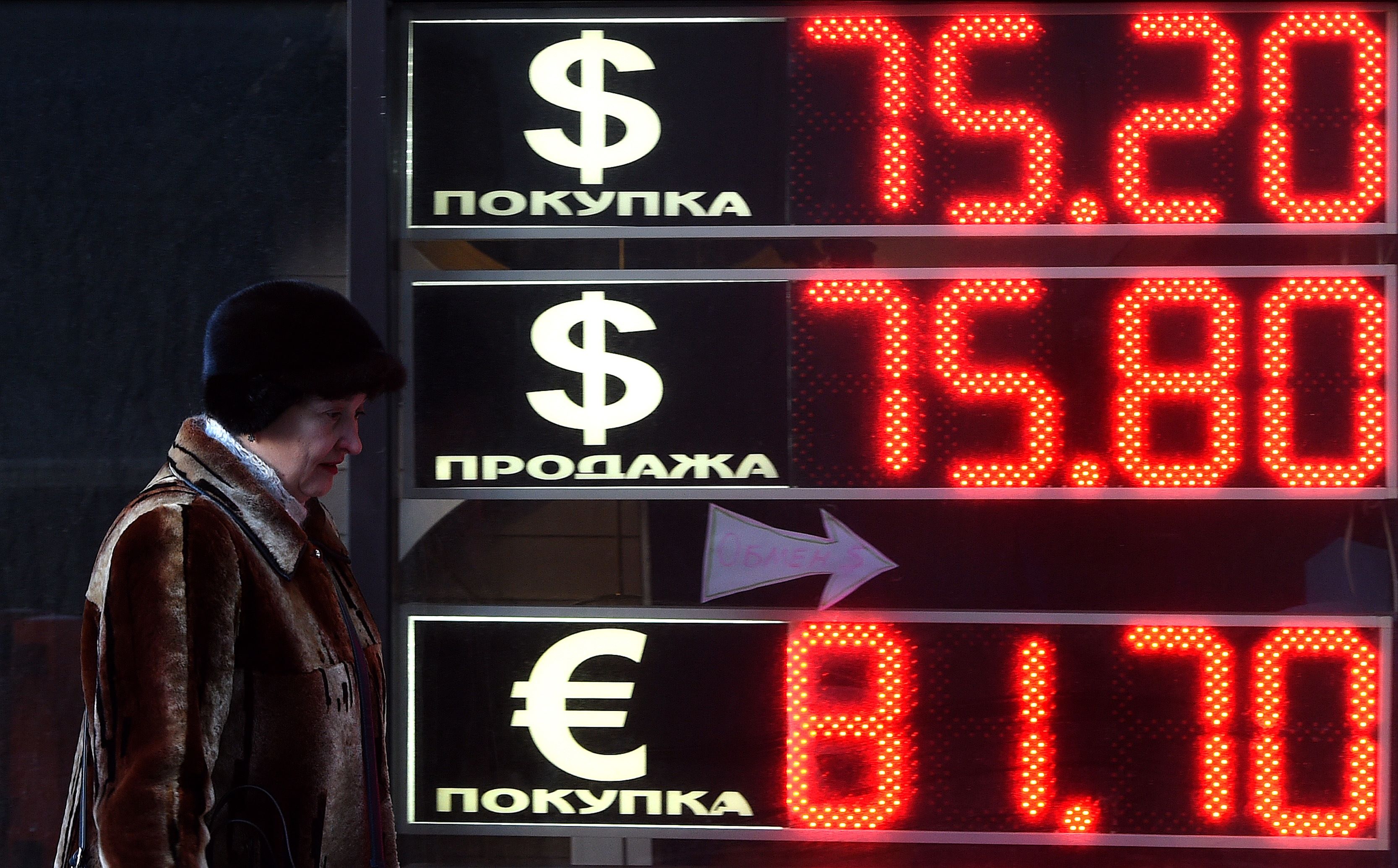 A woman walks past a board listing foreign currency rates against the Russian ruble in Moscow, on January 11, 2016. Russia's battered ruble on January 11 fell to 76 against the dollar and over 83 against the euro for the first time since the currency slump of December 2014. AFP PHOTO / VASILY MAXIMOV
