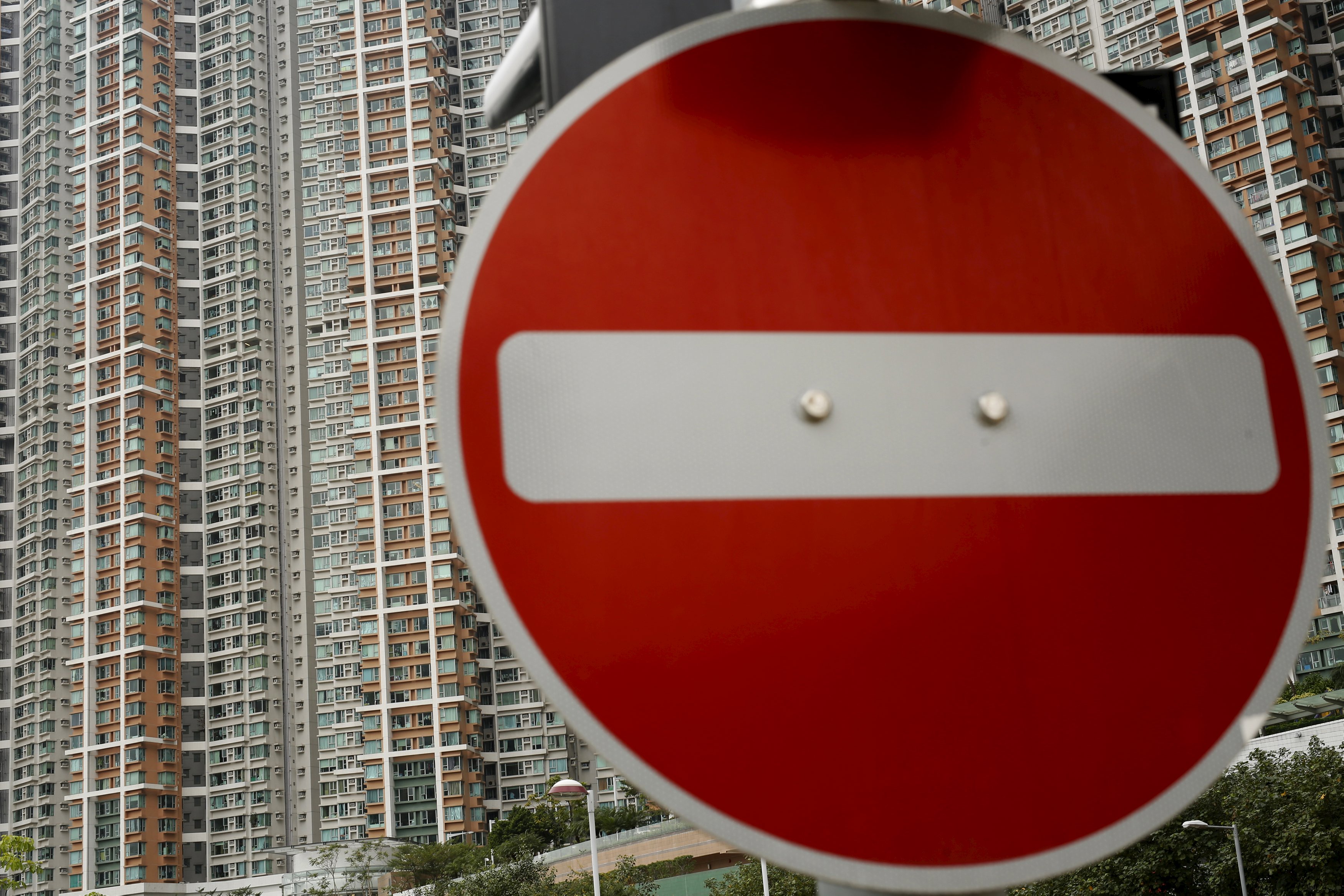 Private housing blocks are seen behind a traffic sign in Hong Kong, China December 15, 2015. Hong Kong is bracing for greater economic challenges as the prospect of a new cycle of interest rate rises drives fears of capital outflows that could put further pressure on the Asian financial hub. Hong Kong's property market, which has seen prices more than double since 2008, had already slowed in anticipation of a local rate hike, and analysts say a further slowdown will depend on China, which is facing its weakest growth in 25 years. Picture taken December 15. REUTERS/Tyrone Siu