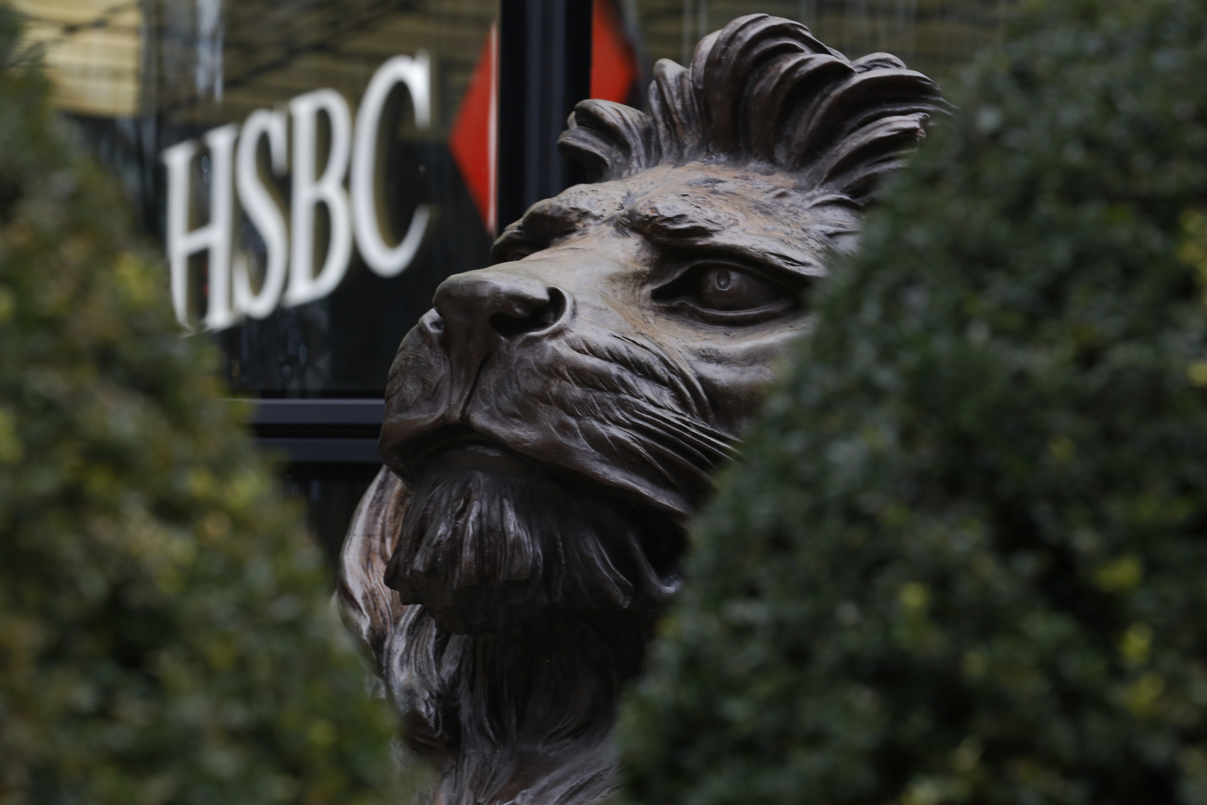 A sculpture of a lion, seen through hedges, sits outside the main entrance to the HSBC Holdings Plc headquarters in the Canary Wharf business, financial and shopping district in London, U.K., on Saturday, Feb. 13, 2016. HSBC's board will meet on Sunday to decide whether to shift its headquarters from London, according to two people with knowledge of the decision. Photographer: Luke MacGregor/Bloomberg