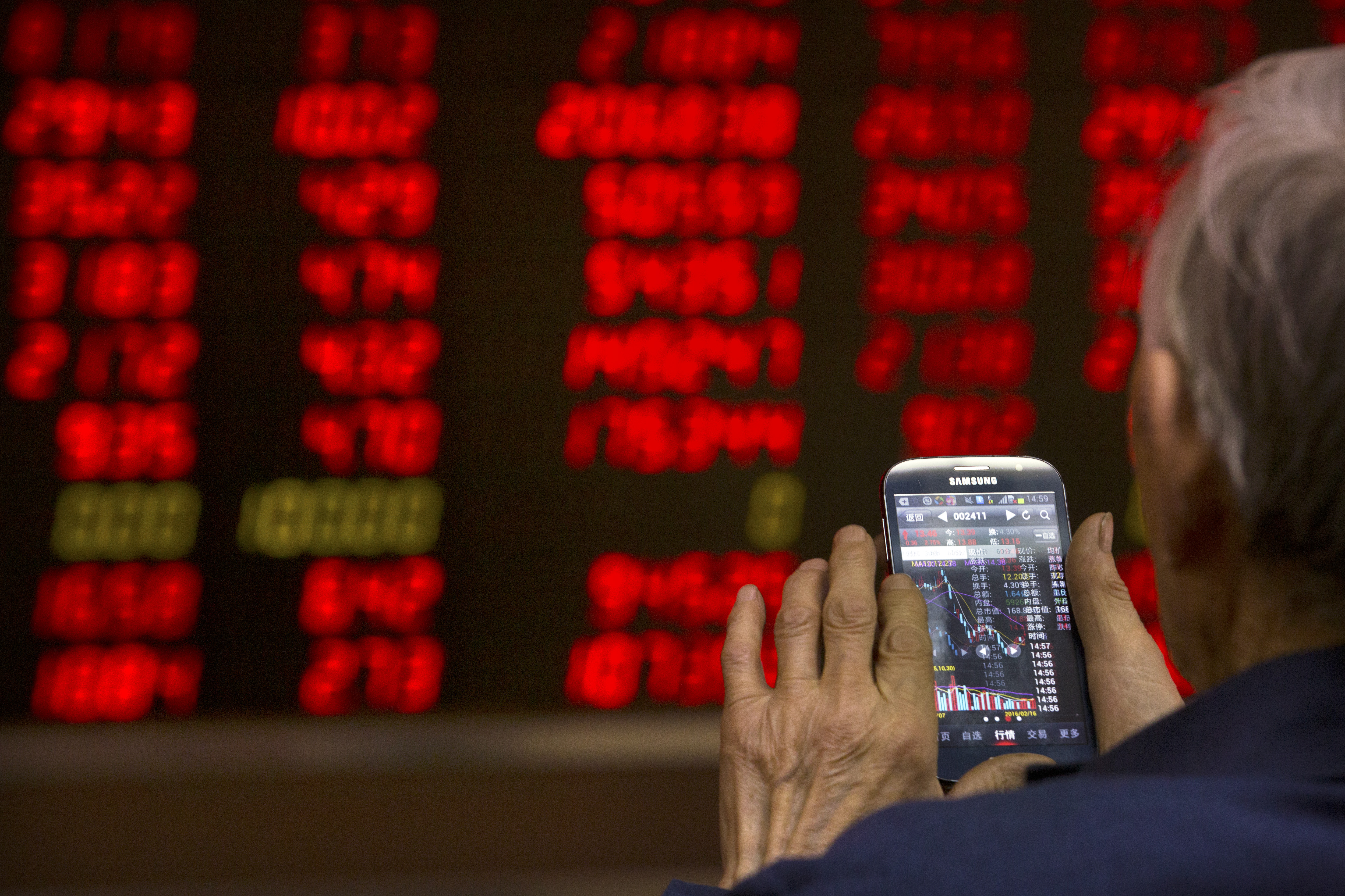 A Chinese investor in Beijing checks stock prices on his phone. Photo: AP