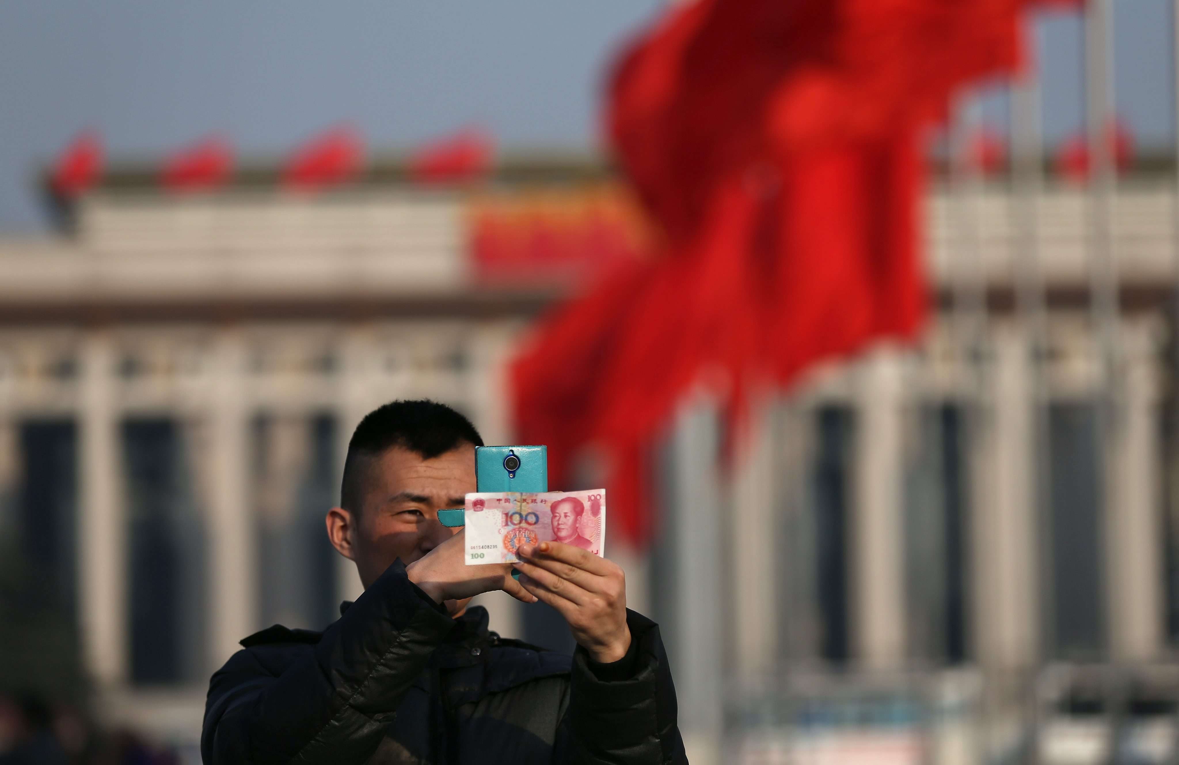 A man photographs a 100-yuan note in Tiananmen Square, Beijing. Photo: EPA