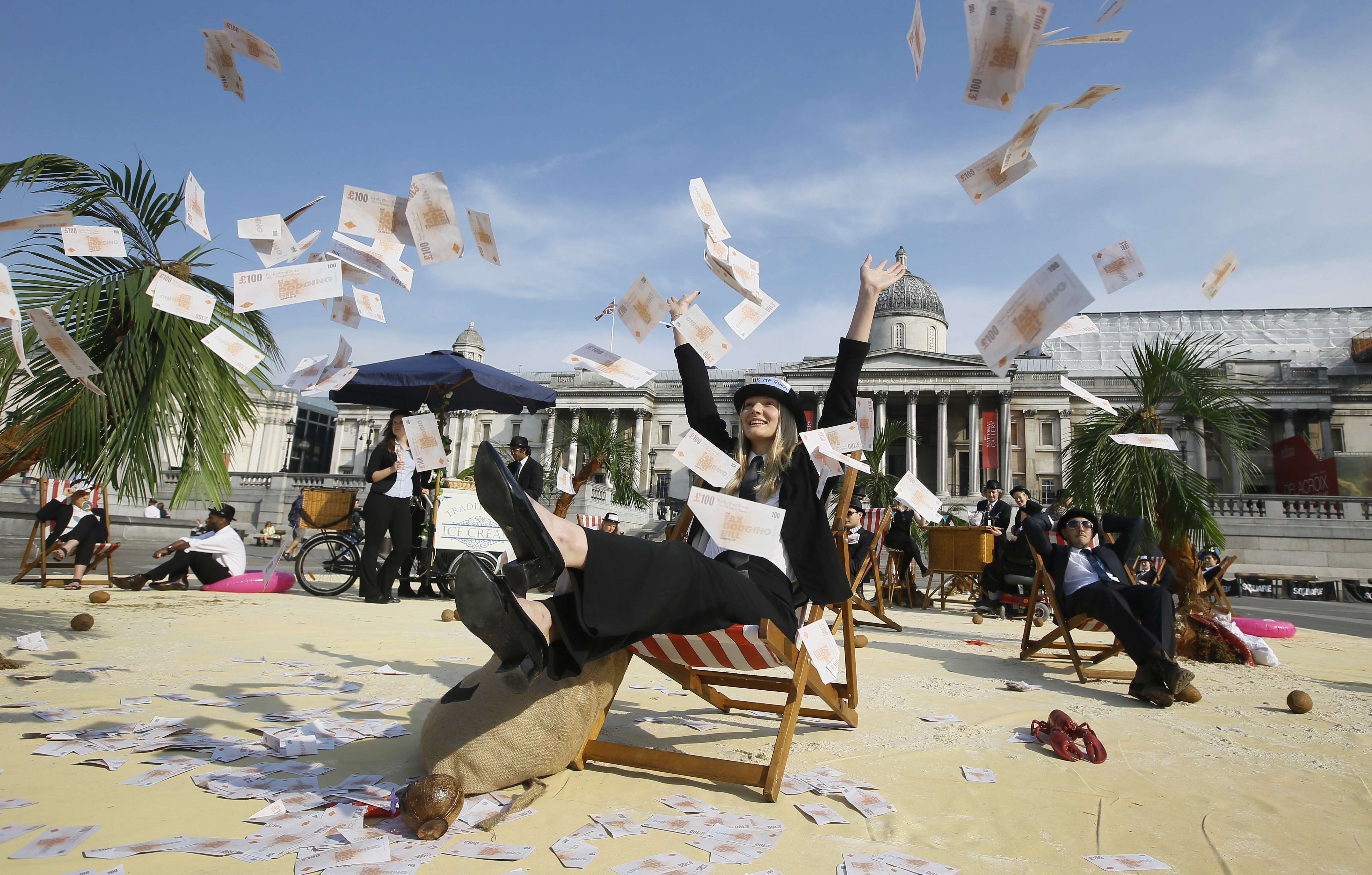 A protester throws fake money into the air in a “tropical tax haven beach” in Trafalgar Square in London. NGOs including Oxfam, Action Aid and Christian Aid are calling for an end to tax havens. Photo: AP