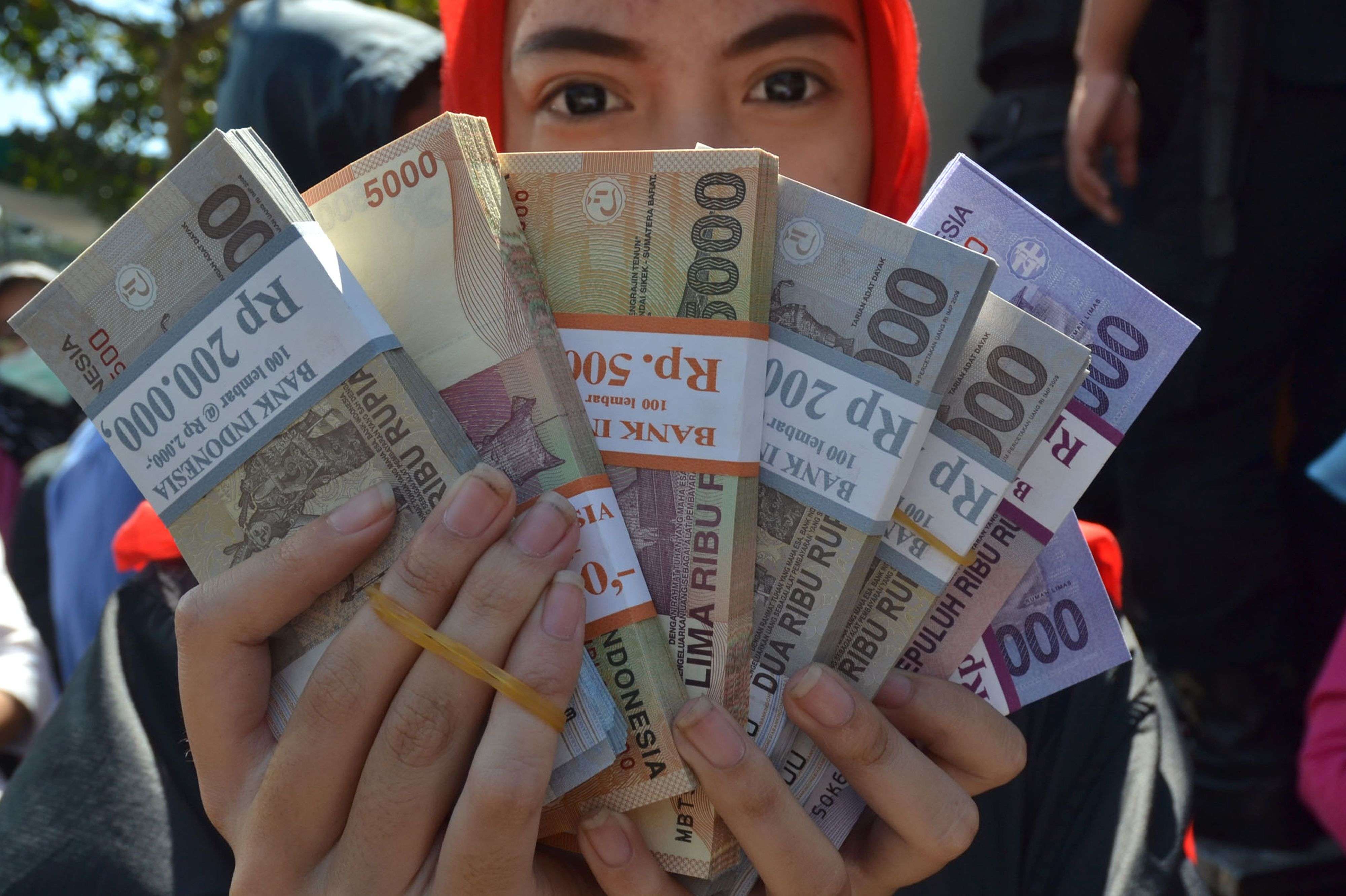 An Indonesian woman holds up rupiah notes she plans to distribute to family members for Eid al-Fitr at the end of the holy month of Ramadan next month. Photo: AFP