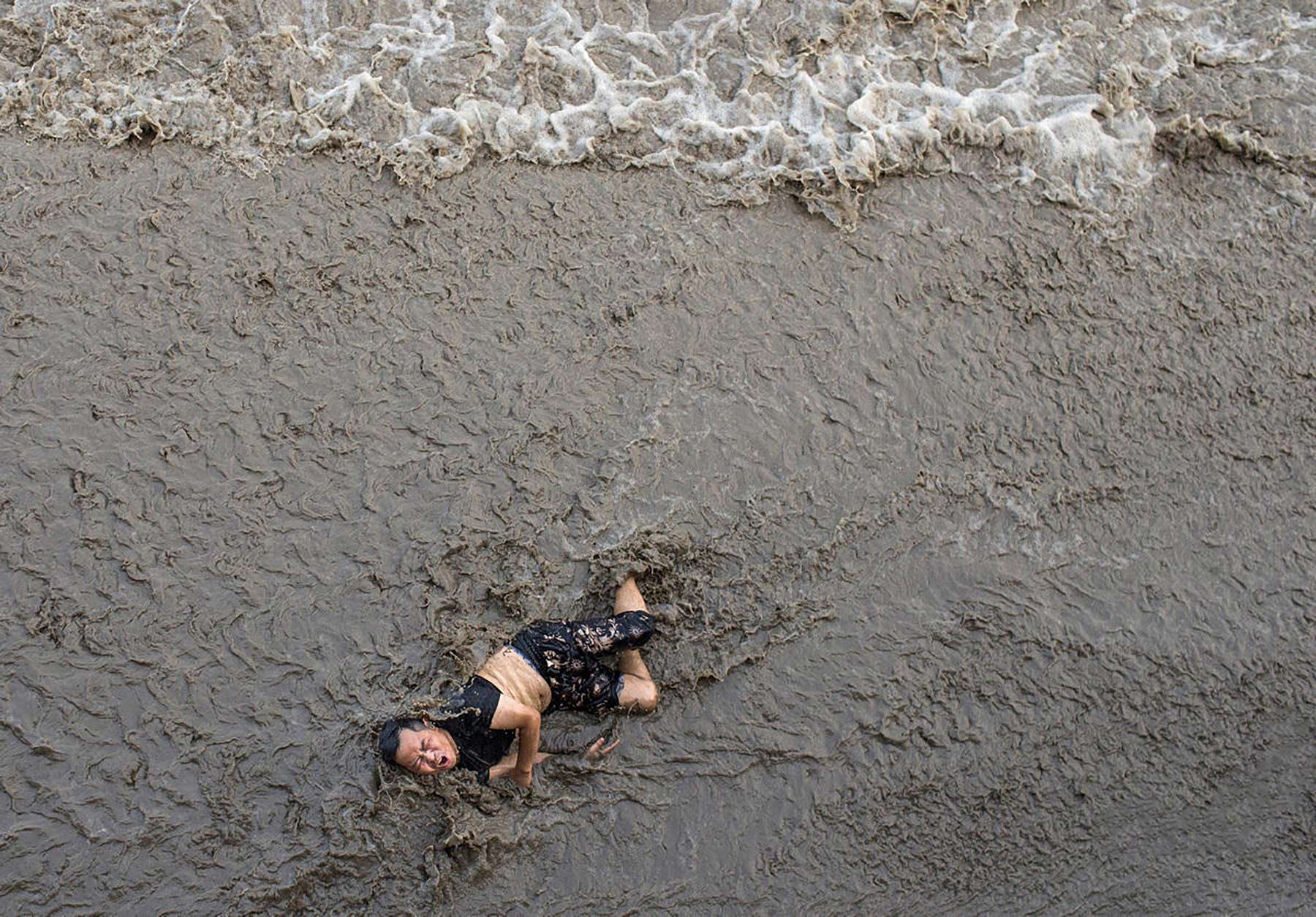 An injured man lies on the edge of the Qiantang River as the water rapidly rises. Photo: SCMP Pictures