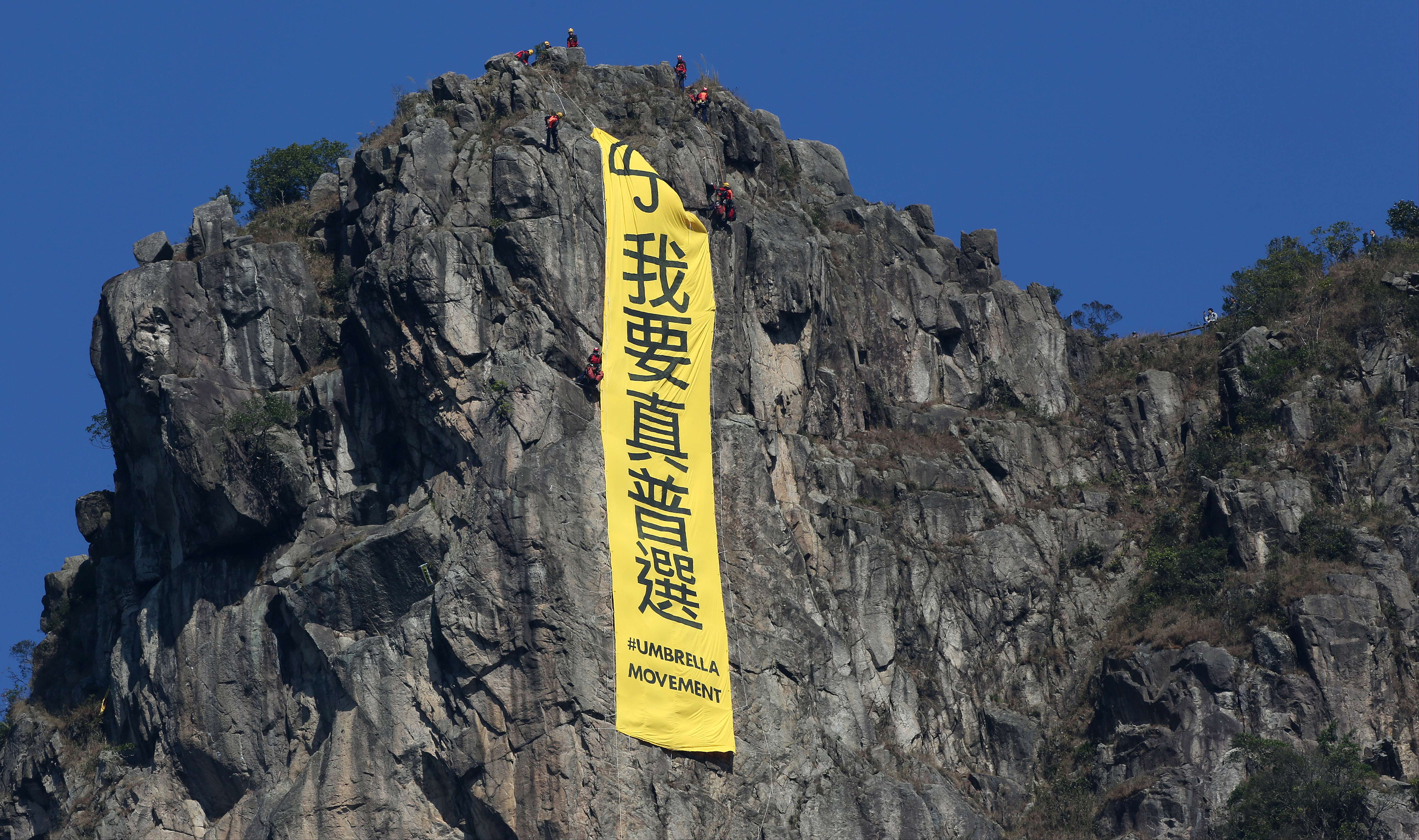 Workers take down a banner demanding “genuine universal suffrage” from atop Lion Rock. Photo: Nora Tam
