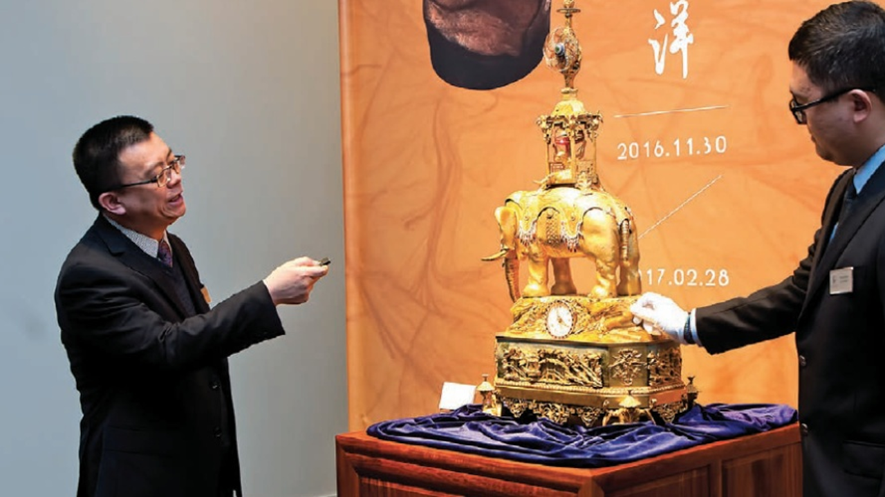 Tour guide Liqun Wan (left) points out the mix of European and Chinese motifs in a gold animatronic clock during the opening of Poly Culture Gallery in downtown Vancouver. Photo: Chung Chow
