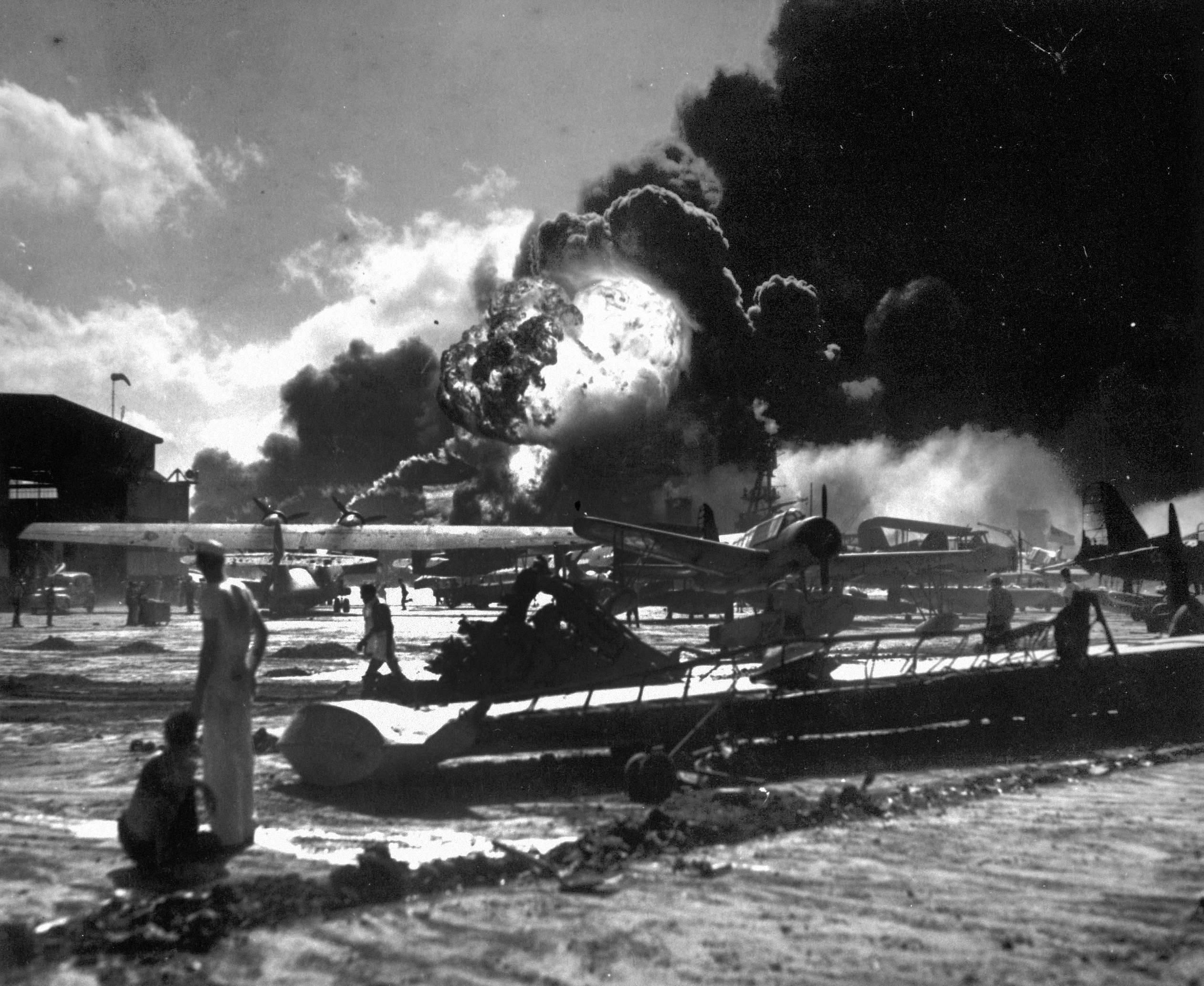 Sailors stand among wrecked airplanes at Ford Island Naval Air Station as they watch the explosion of the USS Shaw, background, during the Japanese surprise attack on Pearl Harbour, Hawaii. Photo: AP