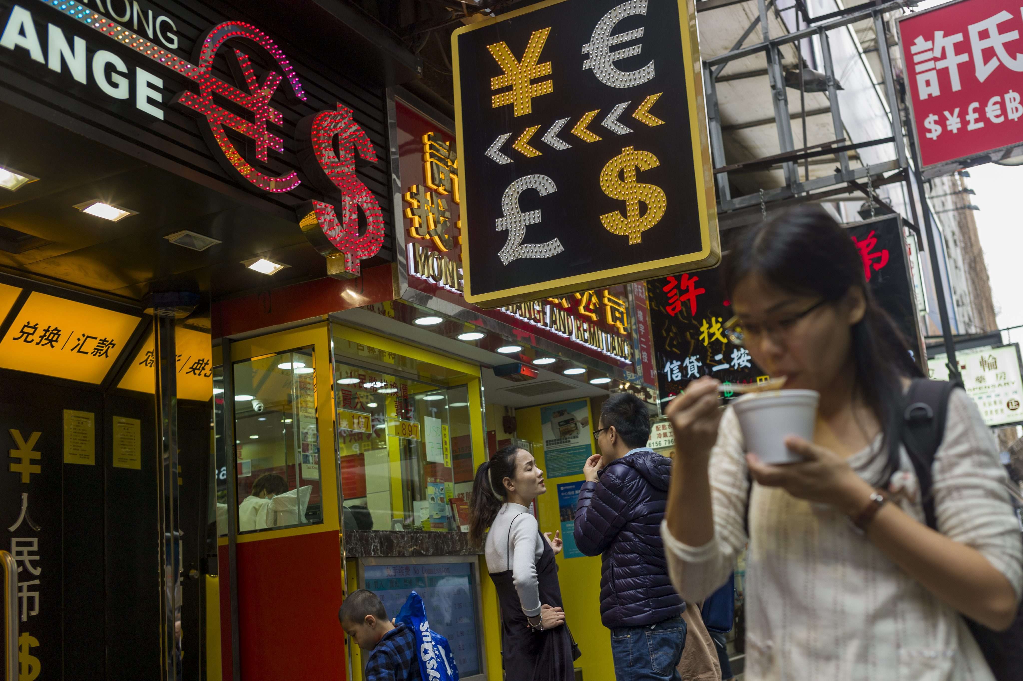 A woman eats instant noodles next to a currency exchange shop in Causeway Bay. Over the past decade, the average income of Hong Kong’s white-collar workers has remained largely unchanged while living costs have surged. As a result, their standard of living has declined. Photo: EPA