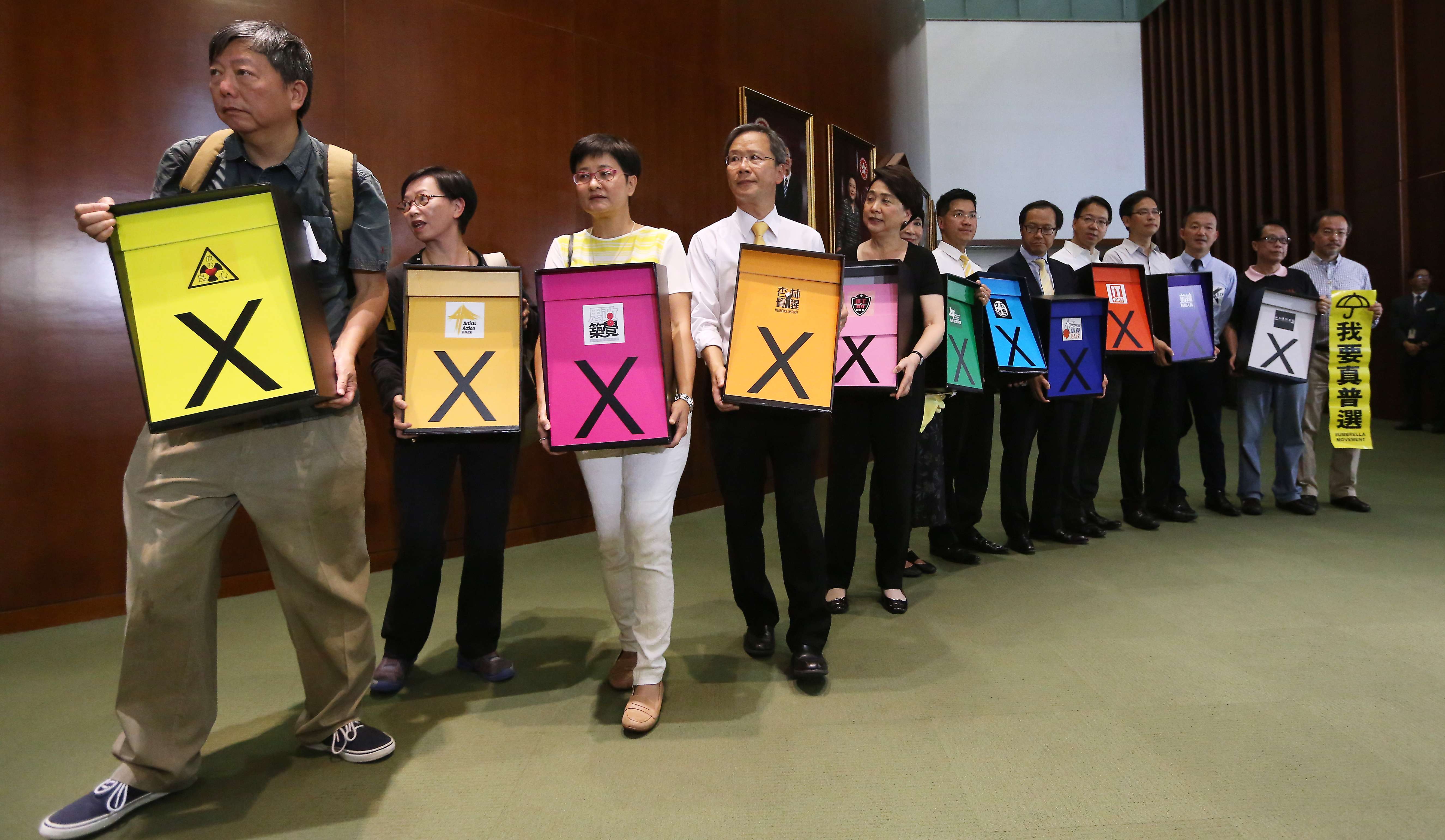 Pan-democrat lawmakers hold signs indicating their stance as they enter the Legislative Council chamber ahead of a debate on the electoral reform proposal, in Tamar on June 17, 2015. The reform package was rejected the following day. Photo: Sam Tsang