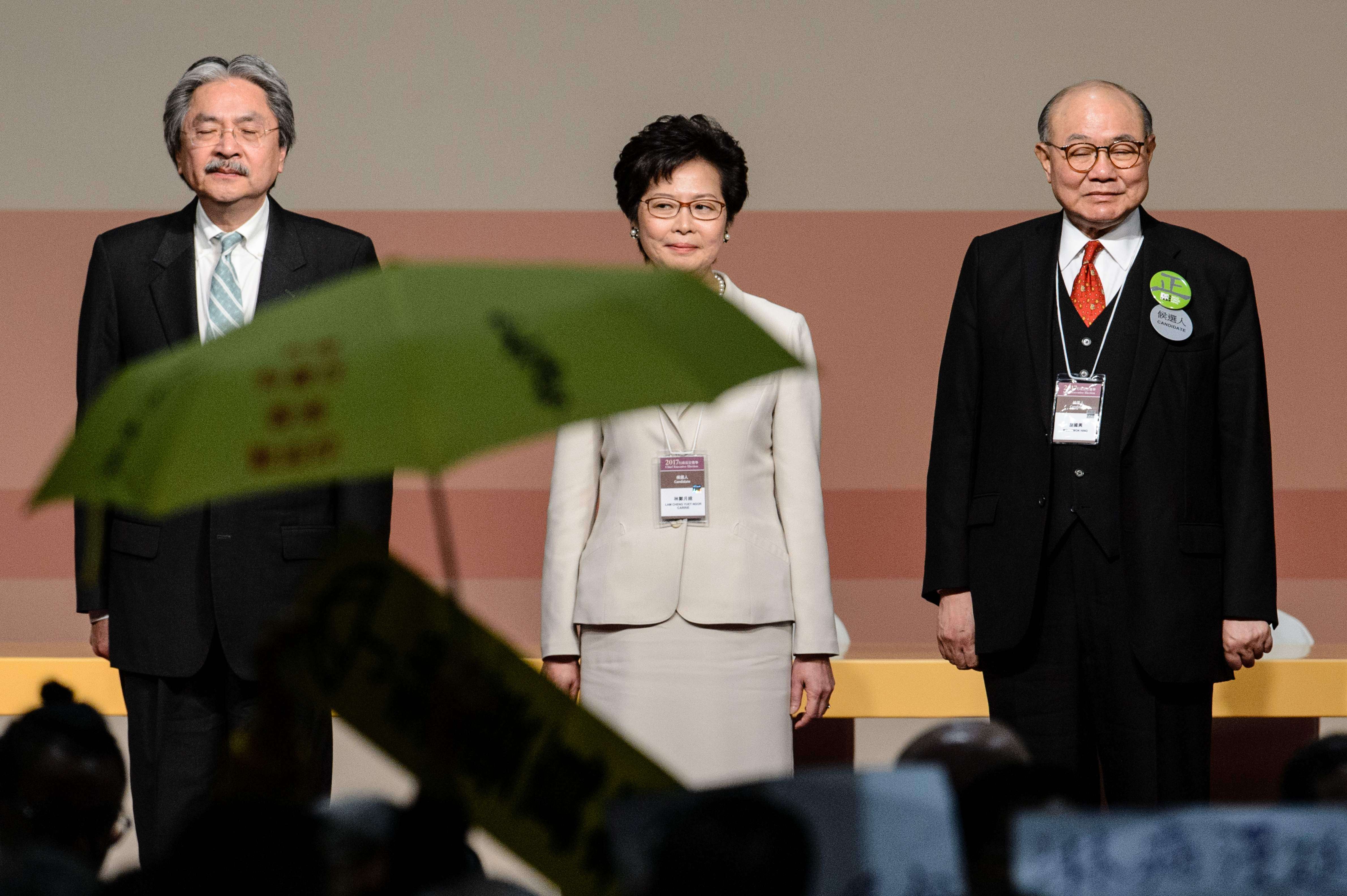A pro-democracy protester holds up an umbrella after Carrie Lam was declared the winner of the chief executive election on March 26, as she stands flanked by losing candidates John Tsang (left) and Woo Kwok-hing. Photo: AFP