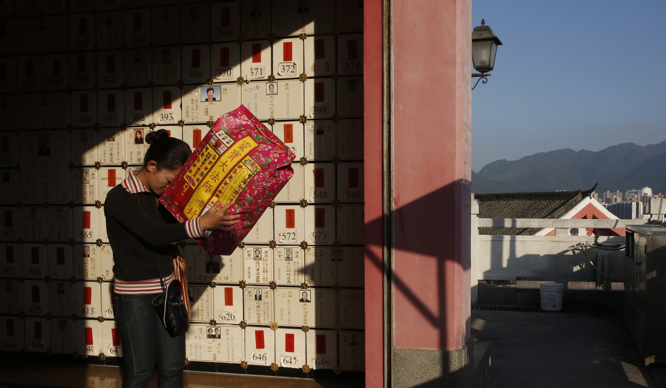 A woman prays with a wall of niches for cremated remains in the background at a private columbarium. Photo: AP