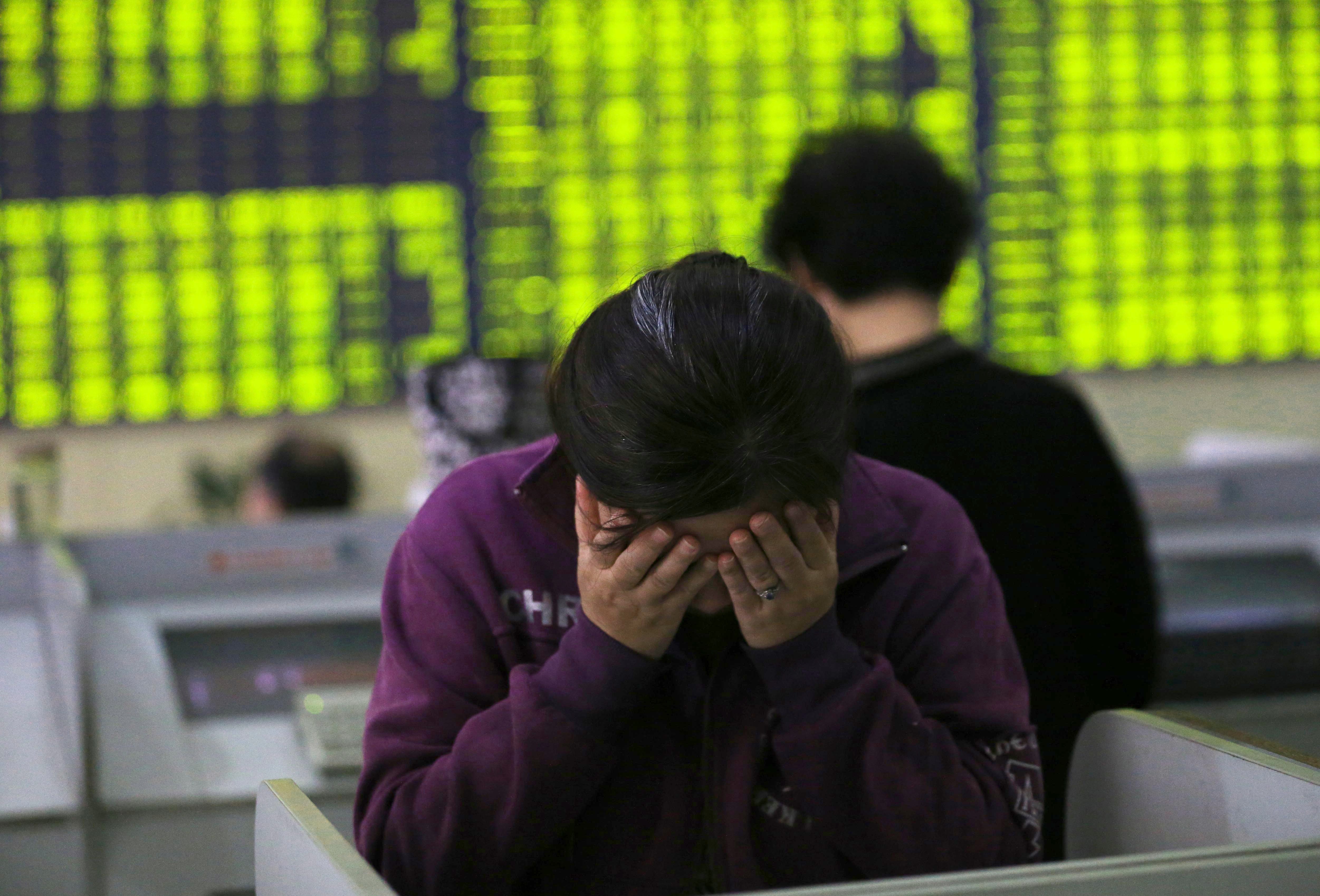 A woman rubs her face as she stands at a computer terminal in a stock brokerage house in Nantong in eastern China's Jiangsu province. Contrary to global conventions, mainland China’s capital market uses green to denote declines, and red to denote advances. Photo: EPA