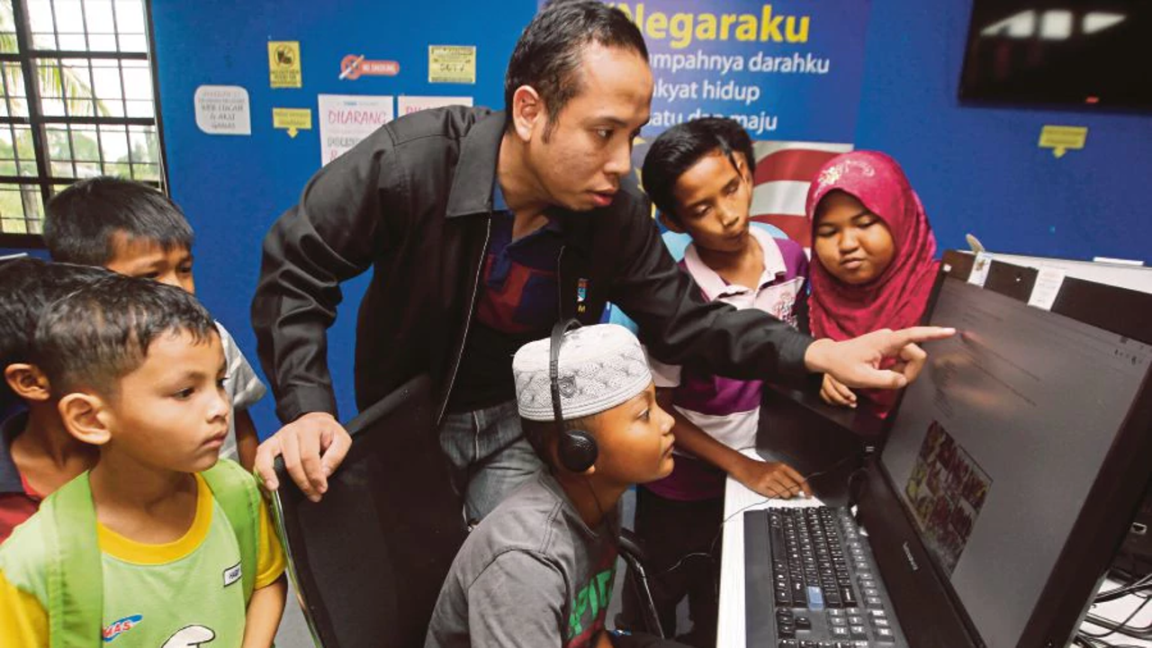 Pusat Internet 1Malaysia manager Mohd Shamsul Mohd Samsuddin (centre) teaching children to use a computer, in Kampung Kempadang, Kuantan. Photo: Farizul Hafiz Awang