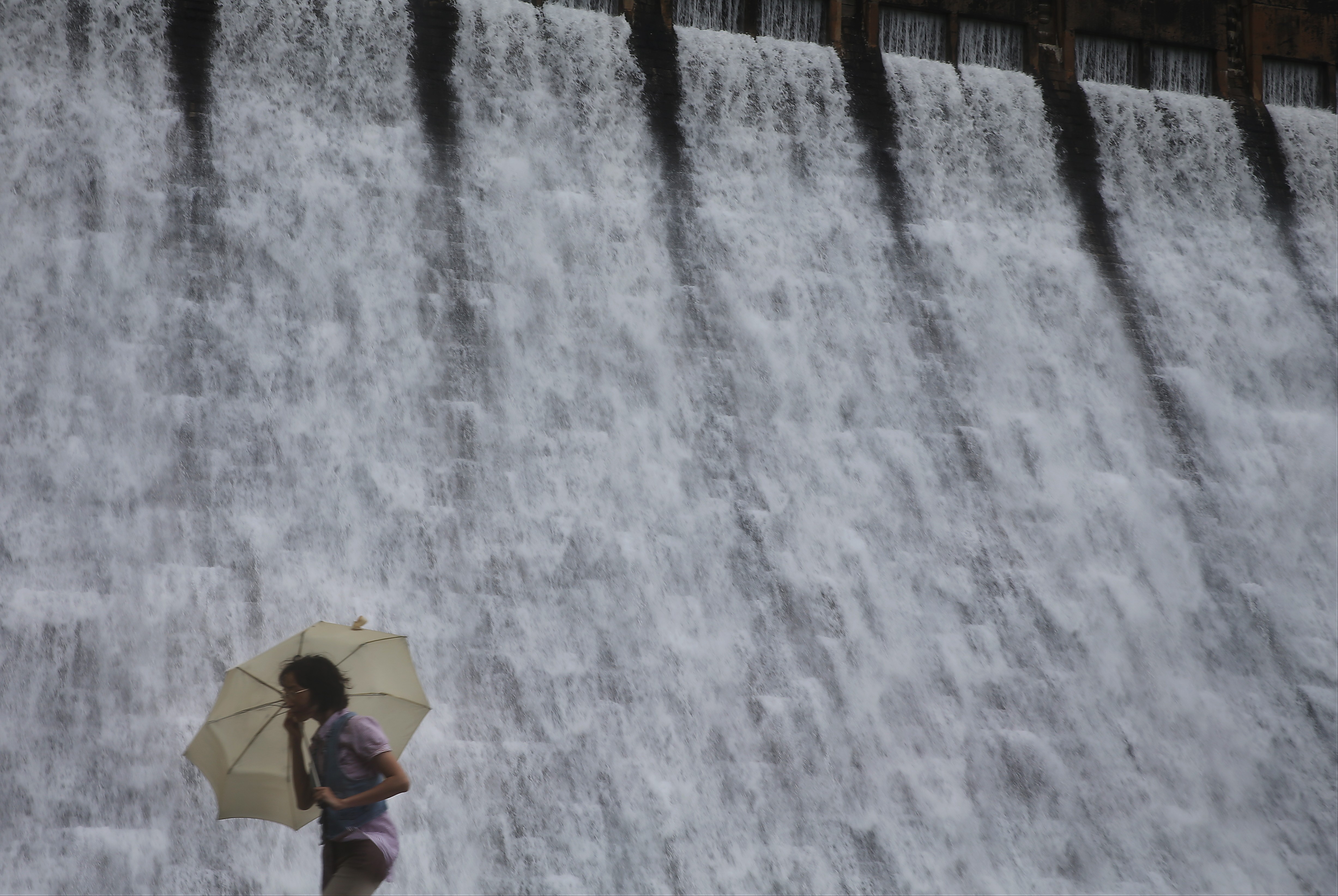 A woman walks past the Tai Tam Tuk Reservoir dam in the rain. For half a century now, the water Hong Kong harvests from rainfall has been insufficient to satisfy local demand. Photo: Sam Tsang
