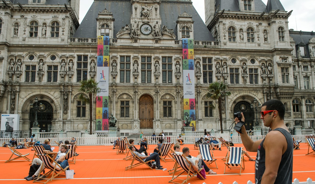 People take a rest on a running track in front of the Paris city hall which displays the 2024 Paris Olympics logo. Photo: EPA