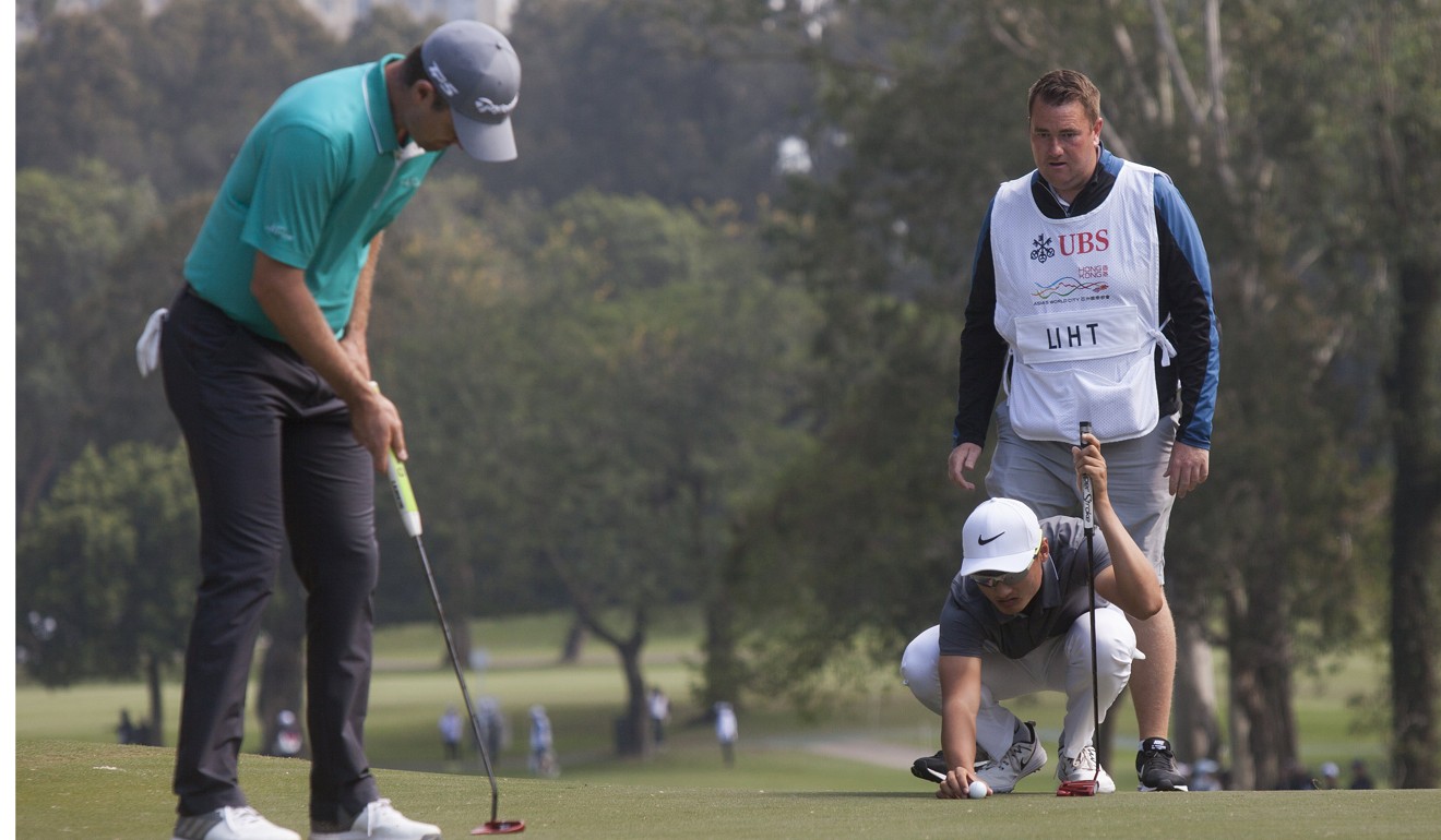 Li Haotong lines up a shot as Justin Rose (left) practices his putt. Photo: EPA