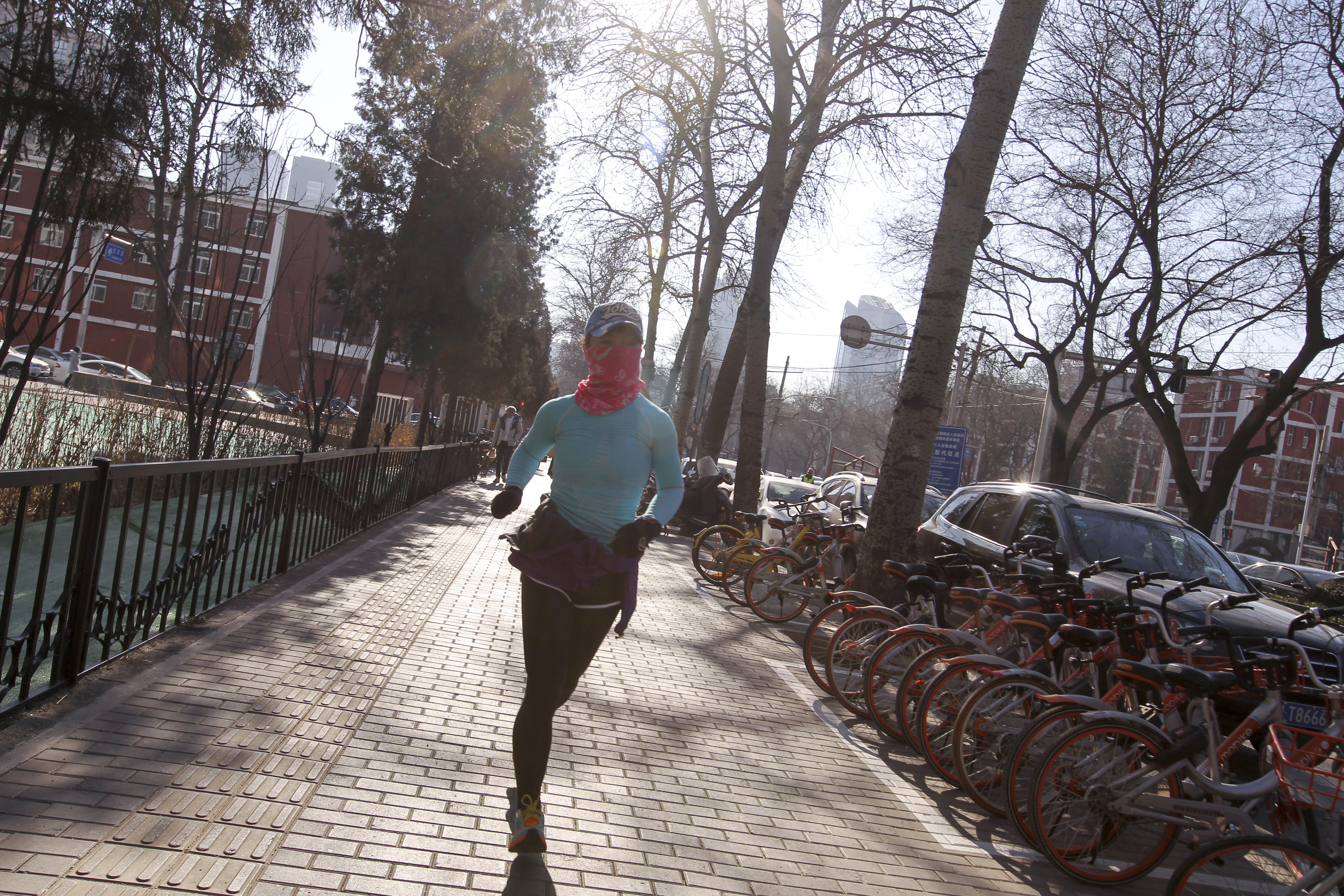 A woman uses a scarf to cover her face as she jogs through Beijing's central business district at noon on Friday. Authorities in the capital earlier issued the first smog alert of the year, saying air quality in the city was set to slump over the coming days. Photo: Simon Song