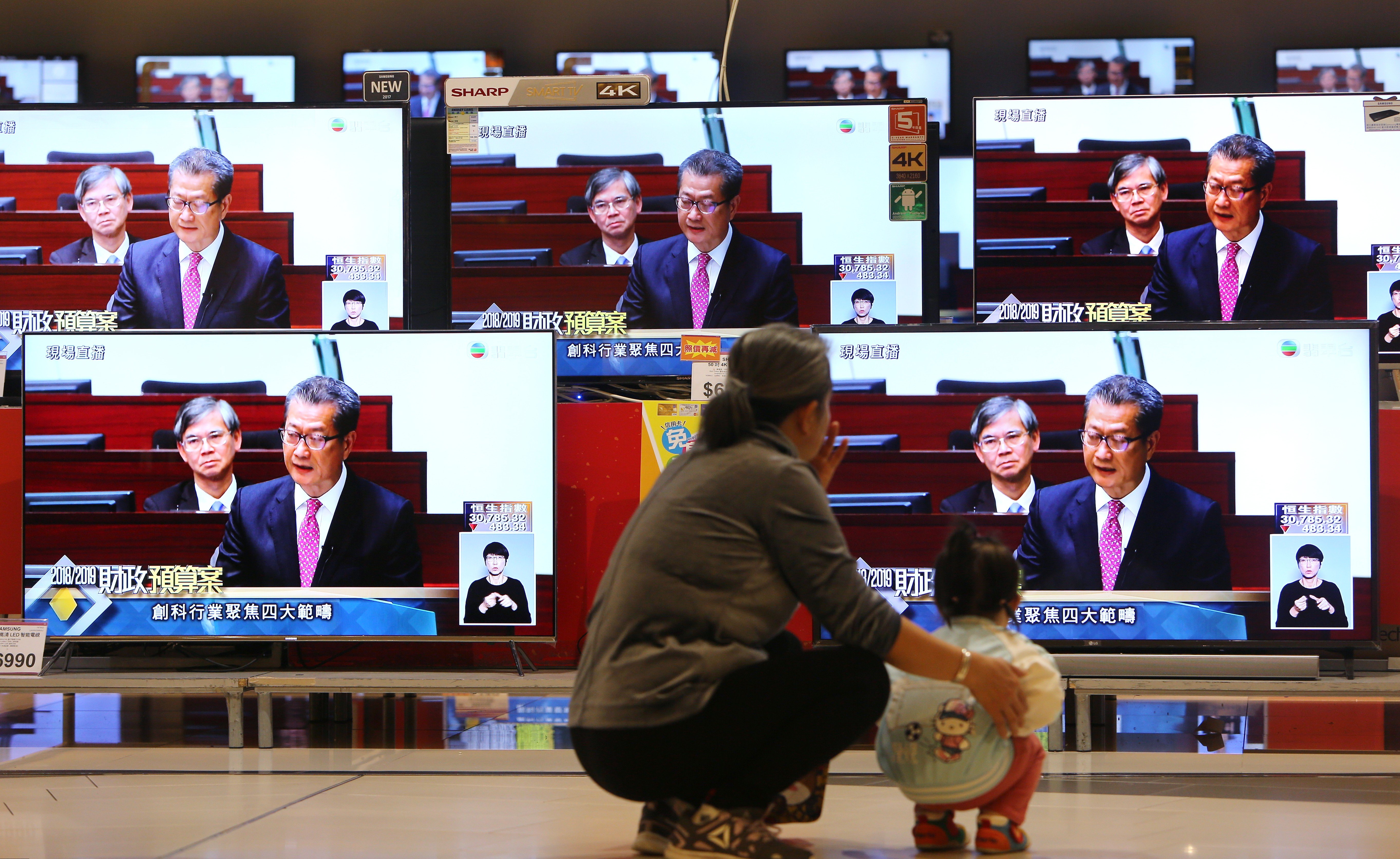 A woman and a child watch the live broadcast of Financial Secretary Paul Chan Mo-po delivering the 2018-2019 budget, in Kowloon Bay. The budget offered tax breaks to the middle-class, but no substantial overhaul of the tax structure. Photo: Winson Wong
