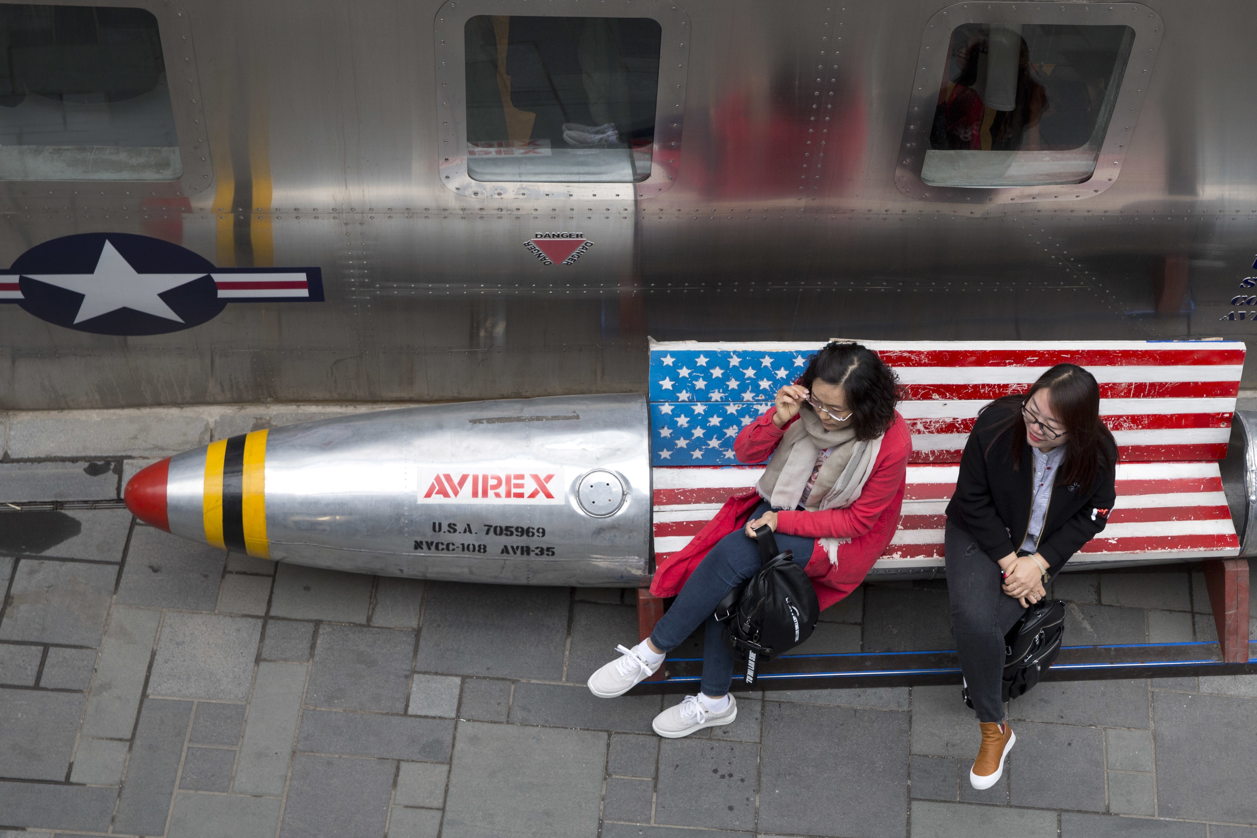 Chinese women sit on a bench with a US flag theme outside an apparel store in Beijing on March 23. China announced a US$3 billion list of US goods including pork, apples and steel pipes that may be hit with higher tariffs in a spiralling trade dispute with President Donald Trump. Photo: AP