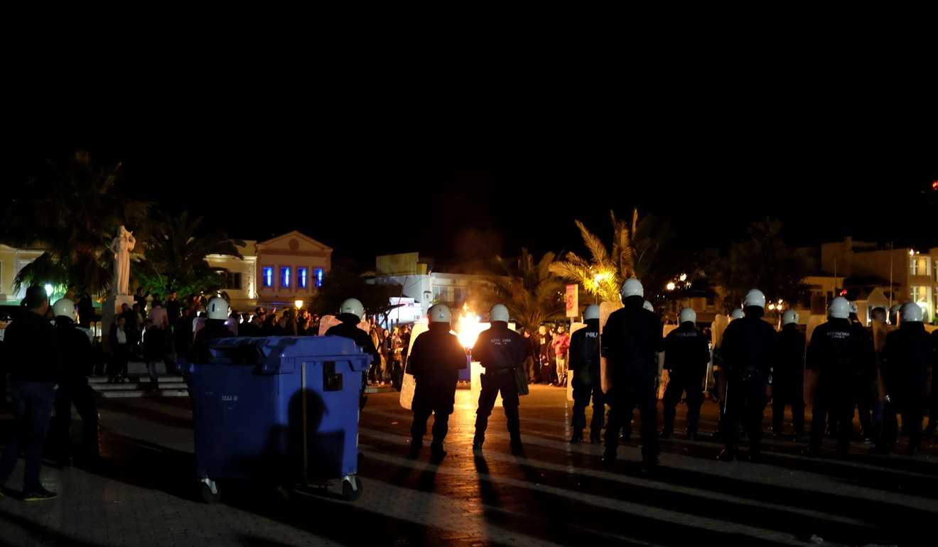 A rubbish bin burns as riot police officers stand guard separating the protesting groups. Photo: Reuters