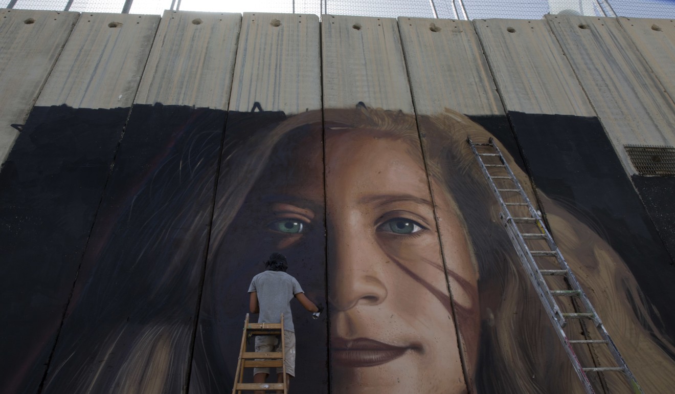 An artist paints a giant mural of prominent Palestinian activist Ahed Tamimi on part of the Israeli separation wall, in the West Bank city of Bethlehem. Photo: AP