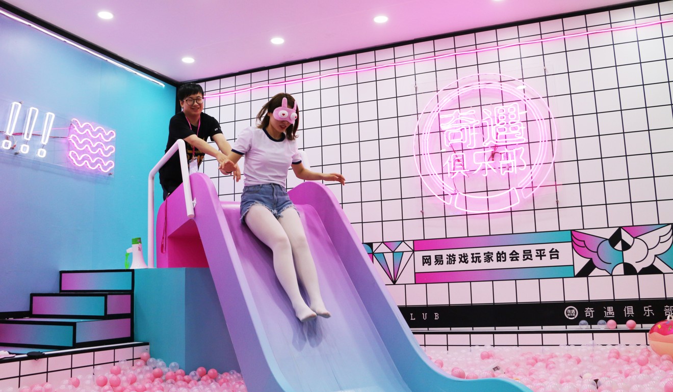 A male attendee helps a showgirl down a slide during a game at the NetEase booth. Photo: SCMP/ Zheping Huang