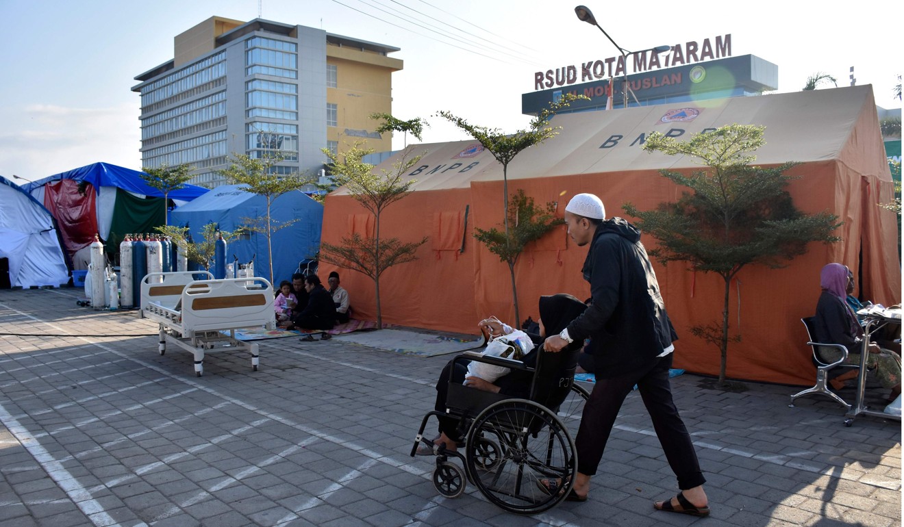 A man pushes his wife in a wheelchair at a makeshift hospital ward in Mataram on Lombok. Photo: AFP