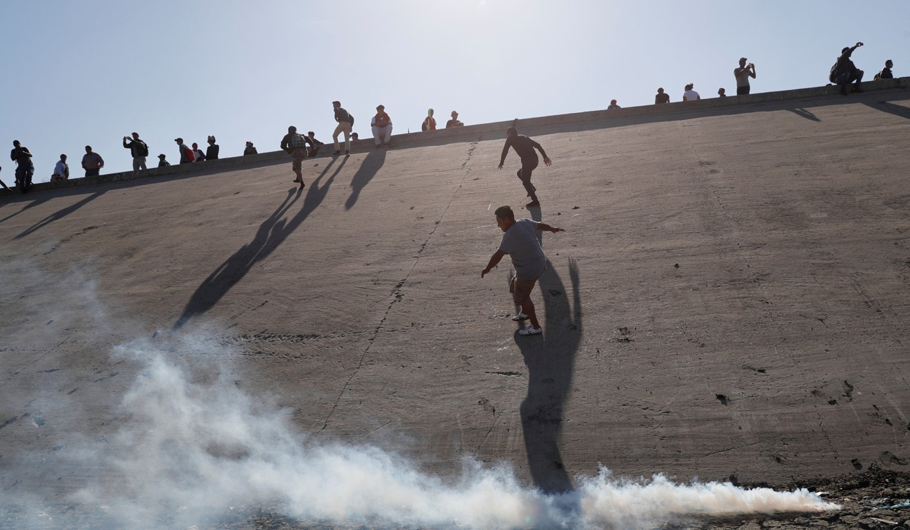 Migrants, part of a caravan of thousands travelling from Central America en route to the United States, run away from tear gas near the border wall between the US and Mexico in Tijuana, Mexico. Photo: Reuters