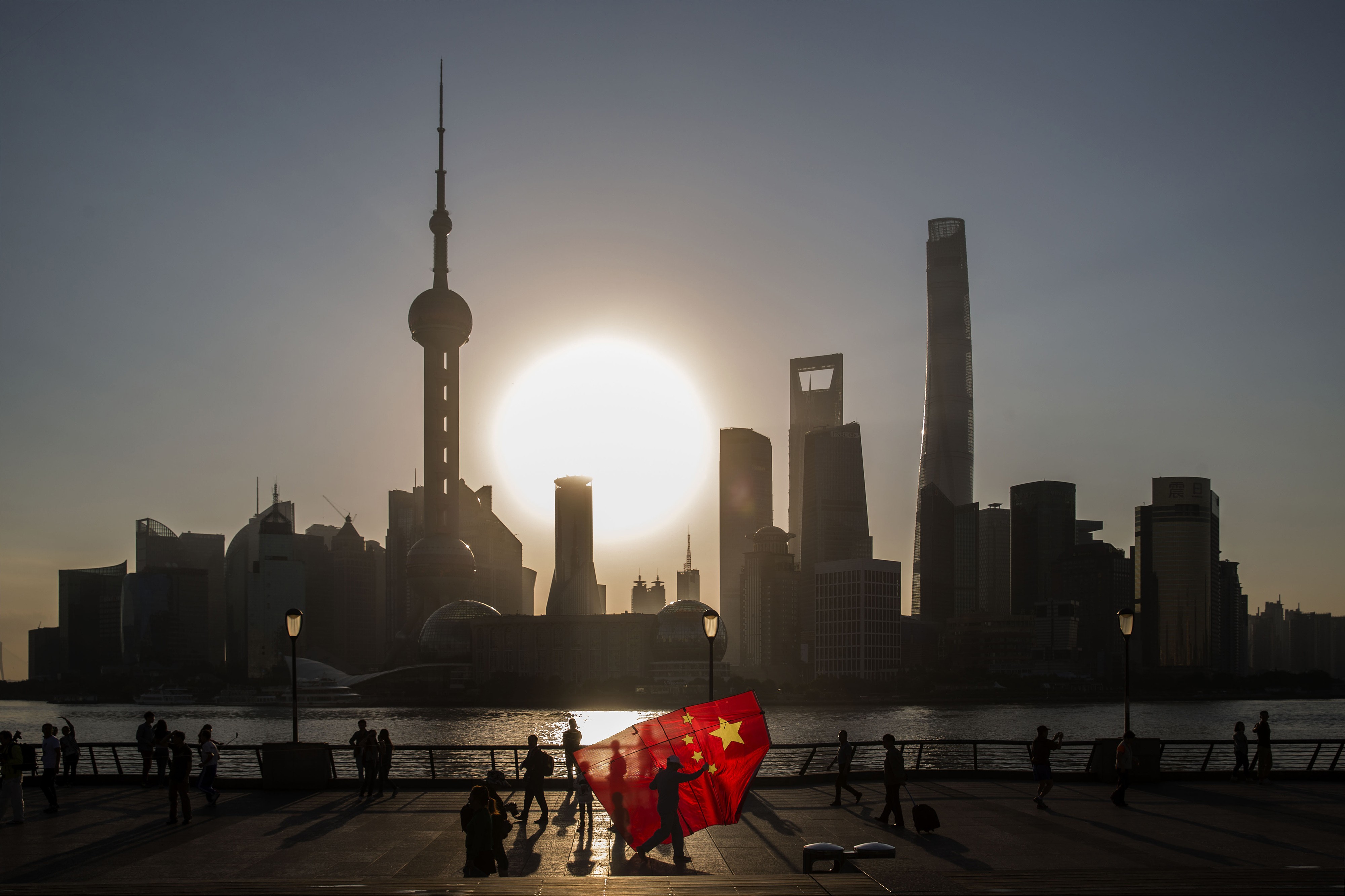 A man carrying a kite in the form of the Chinese national flag walks along the Bund, as the sun rises over the buildings of Pudong's Lujiazui financial district, across the Huangpu River, in Shanghai. Photo: Bloomberg