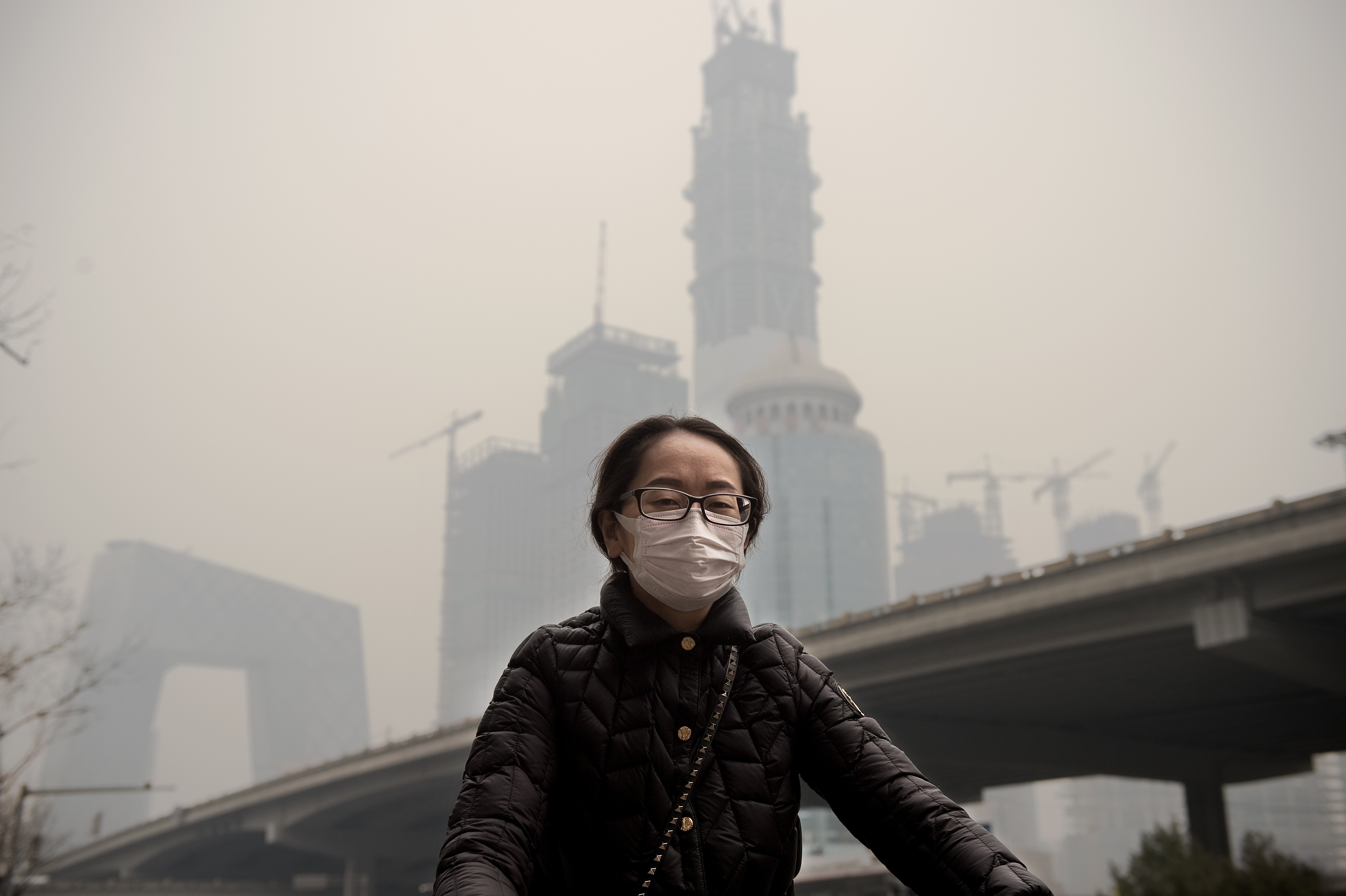 A woman wearing a protective pollution mask rides a bicycle in Beijing on March 20, 2017, when the last large coal-fired power plant in the city suspended operations. China’s real estate companies are now coming together to green their supply chains. Photo: AFP