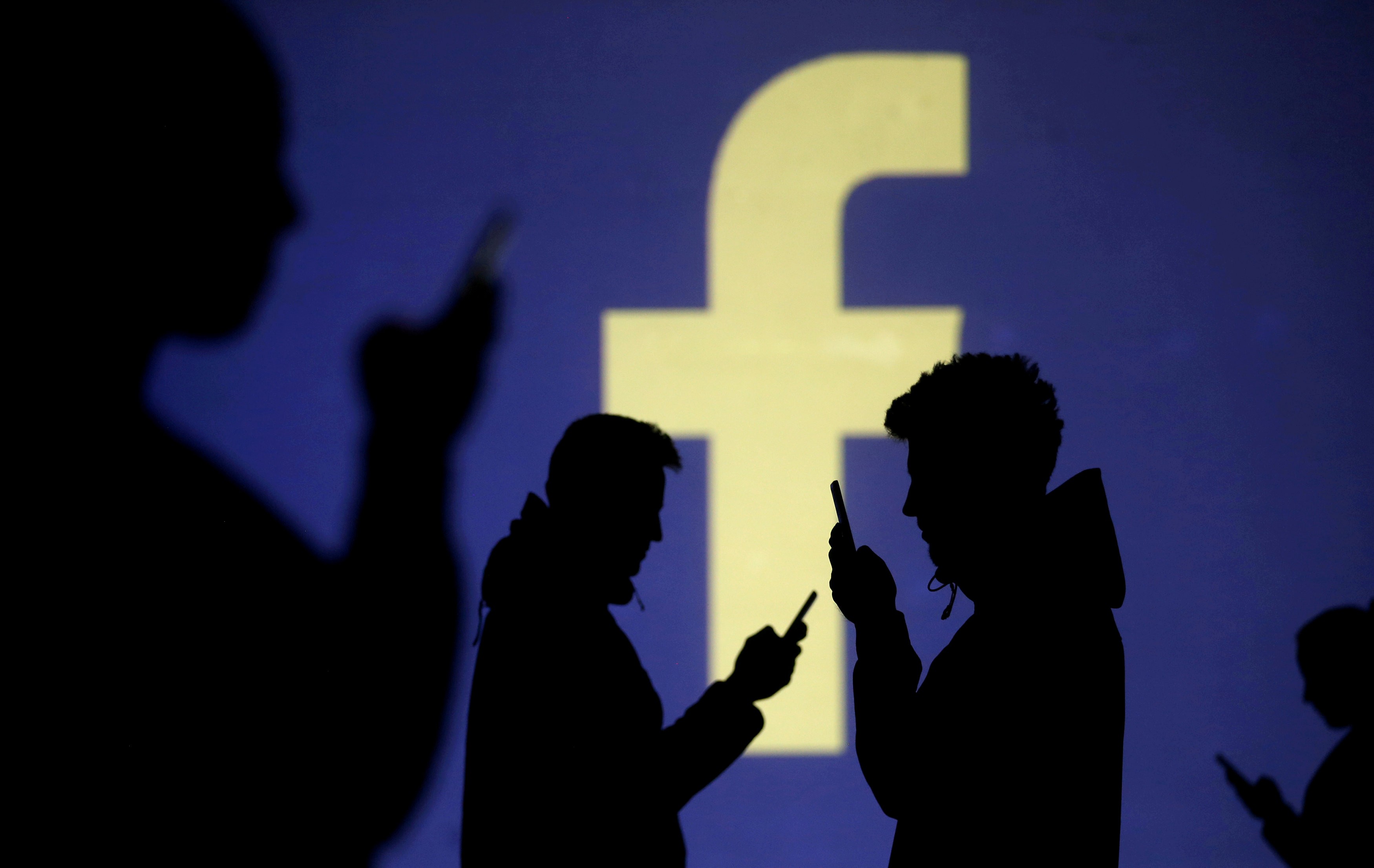 FILE PHOTO: Silhouettes of mobile users are seen next to a screen projection of Facebook logo in this picture illustration taken March 28, 2018. REUTERS/Dado Ruvic/Illustration/File Photo