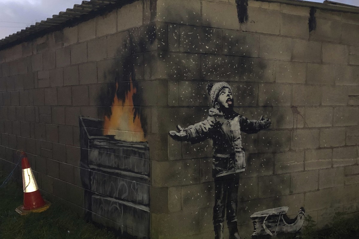 New Banksy Artwork Brings Crowds To Welsh Steel Town Of Port Talbot - mural shows a small boy wrapped up against the cold with his tongue stuck out and
