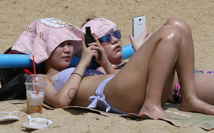 Why not both? Sunbathers work on their tan while using their mobile devices. Photo: Nora Tam